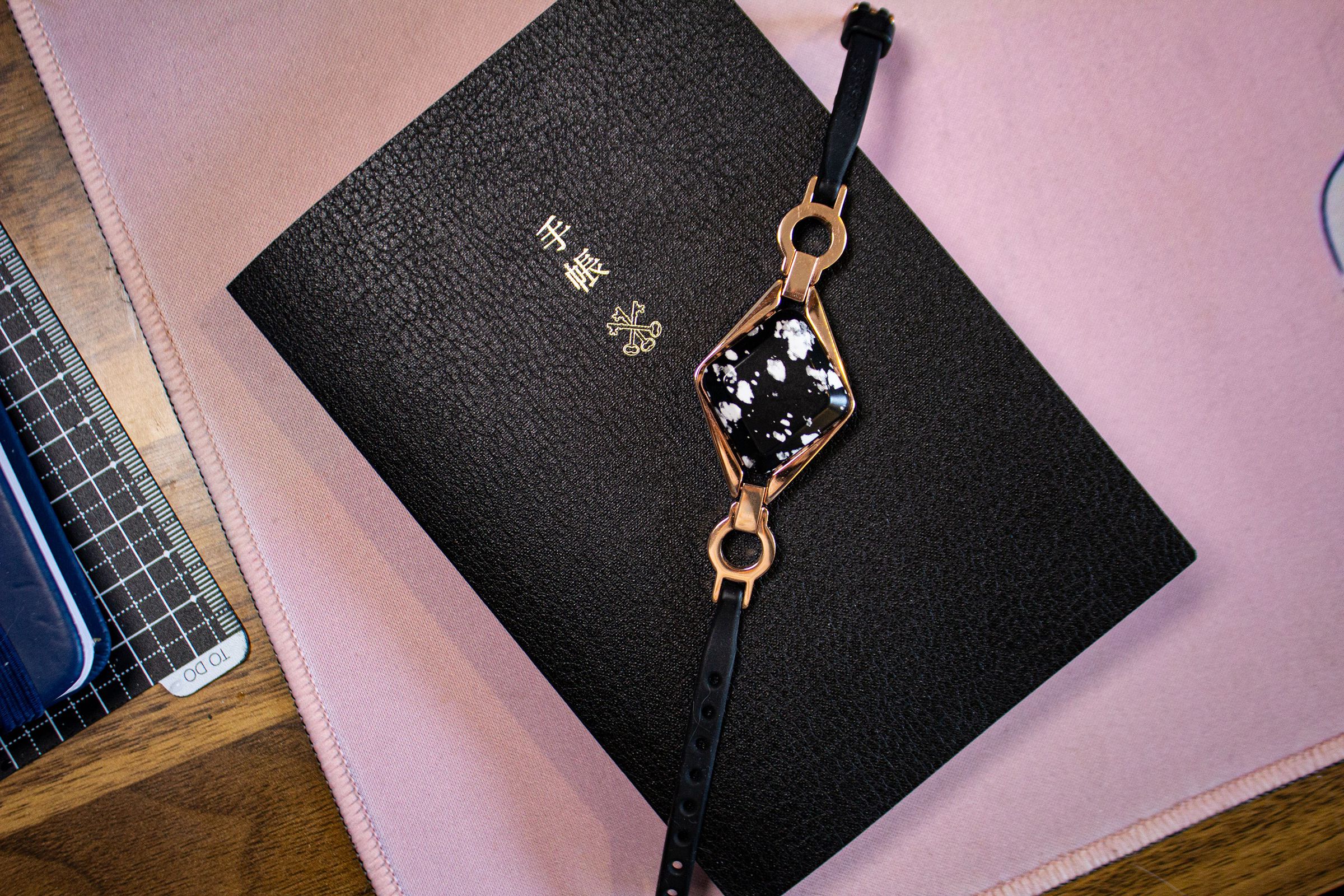 Bellabeat Ivy with black and white stone and rose gold lugs on top of a black notebook and pink desk pad