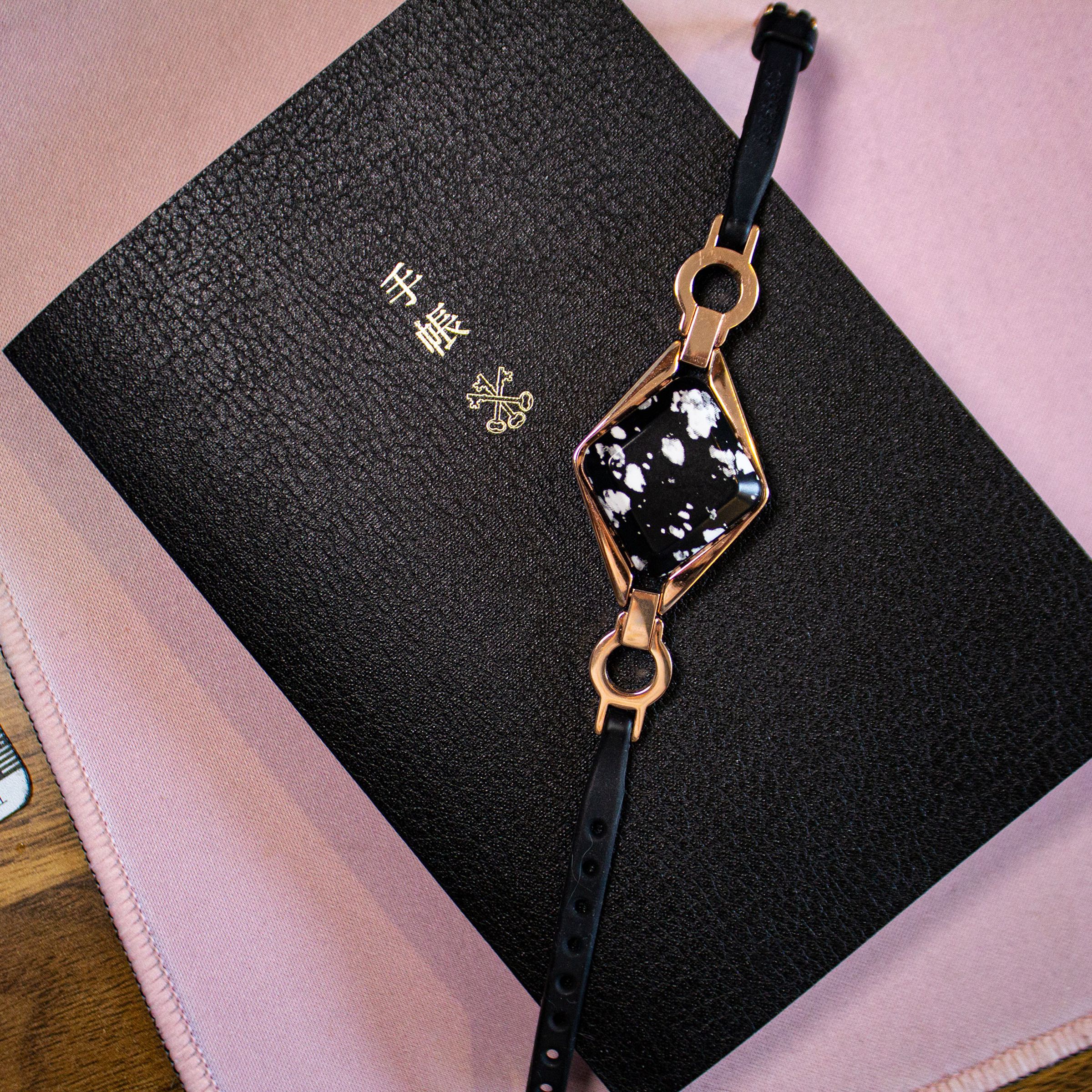 Bellabeat Ivy with black and white stone and rose gold lugs on top of a black notebook and pink desk pad