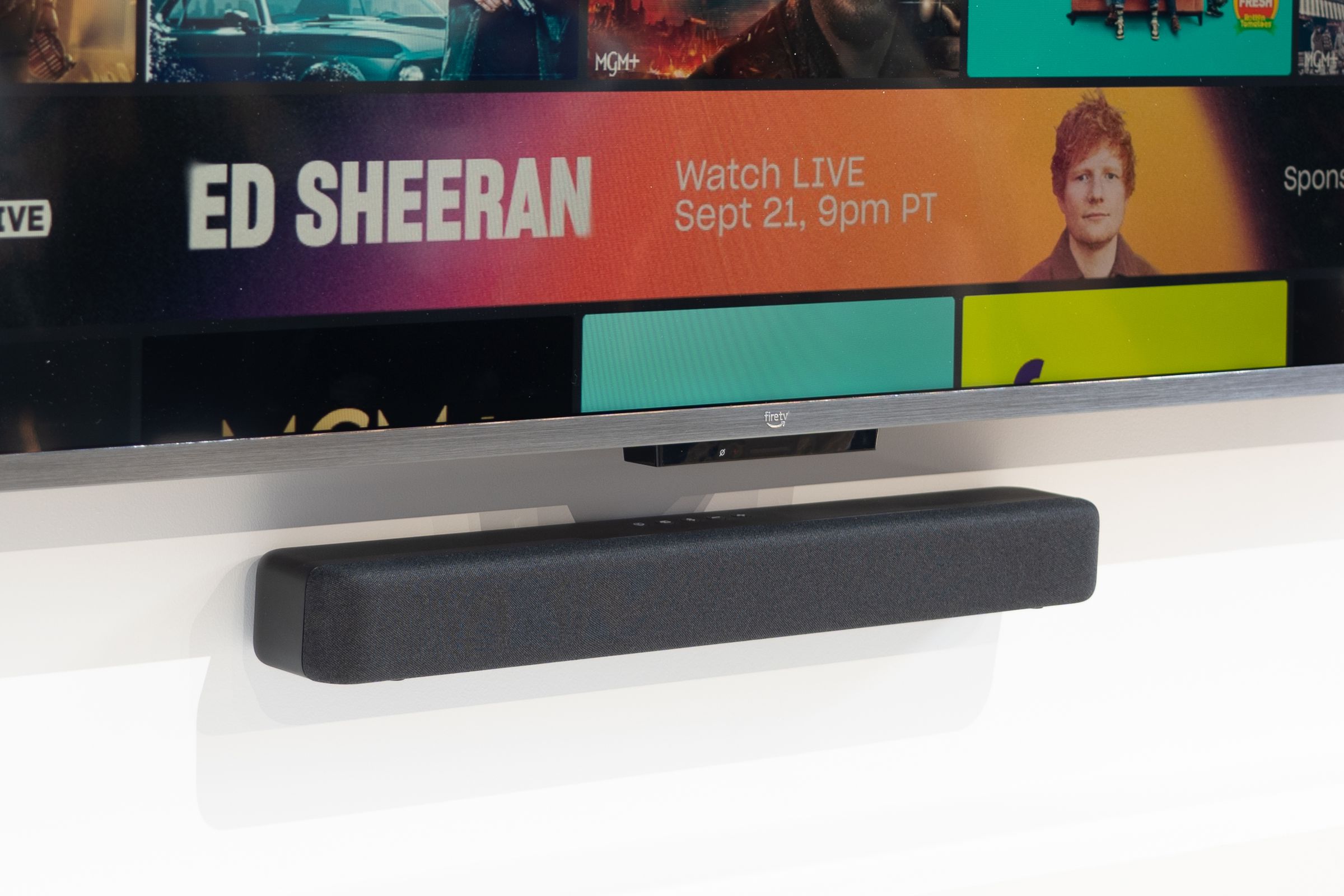 An image of a small black soundbar mounted on a wall beneath a TV.