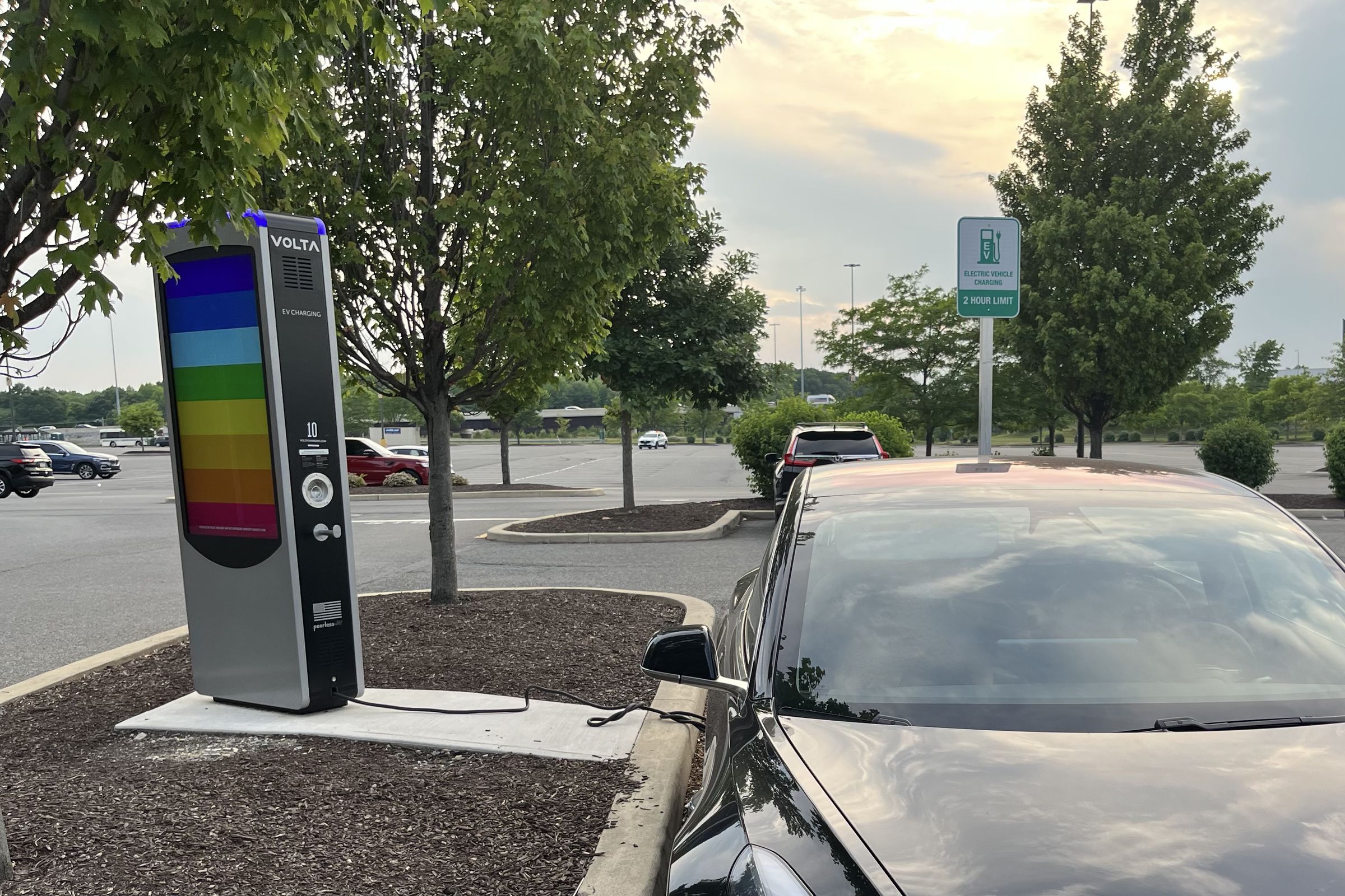 a black Tesla parked in a lot with a Volta charger and rainbow colors on the Volta charging screen