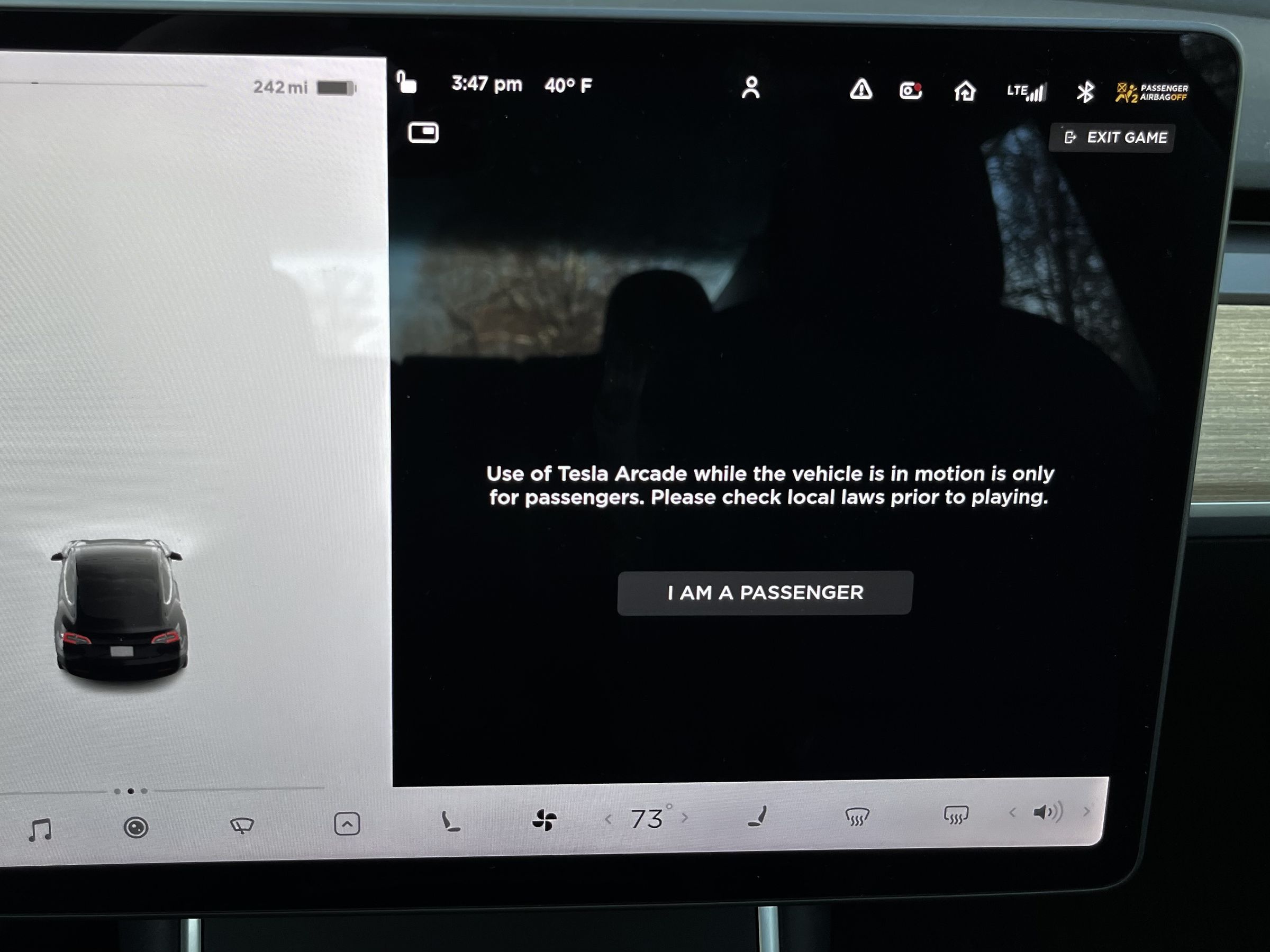 The Tesla center screen is displaying the warning prompt on a black background to confirm you are a passenger, allowing you to tap a button to continue the game.
