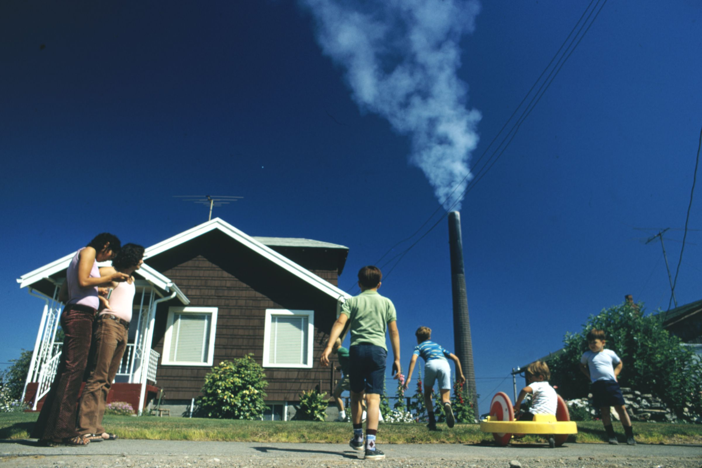 Children play in the yard of a home in Ruston, Washington, while a smelter stack showers the area with arsenic and lead residue in 1972.