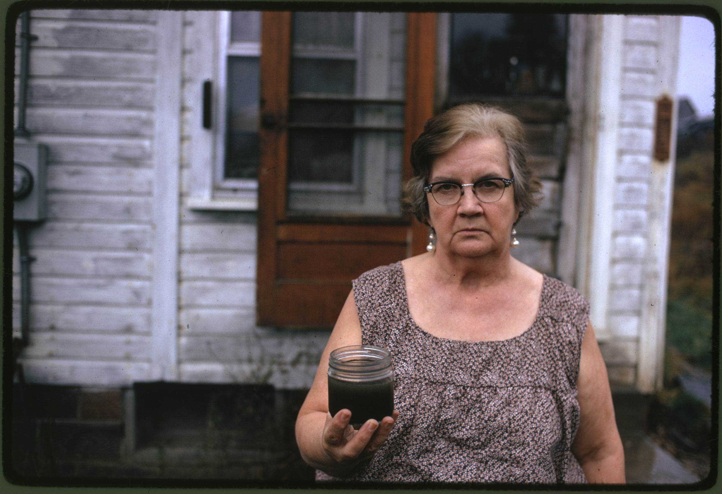 A woman holds a jar of undrinkable water from her well in Ohio in 1973. She filed a damage suit against the Hanna Coal Company, which owned the land around her house.