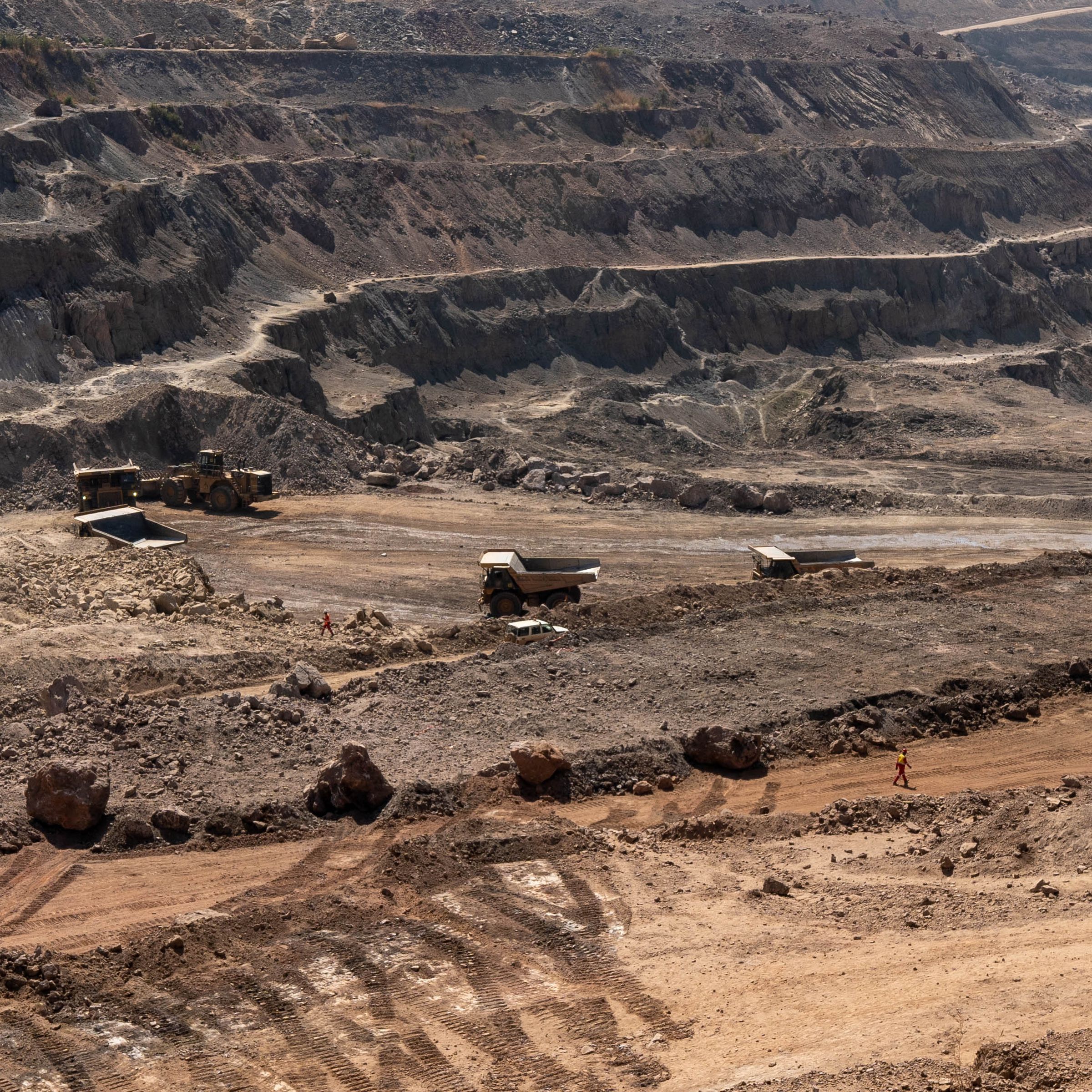 Trucks drive across an open-pit mine.