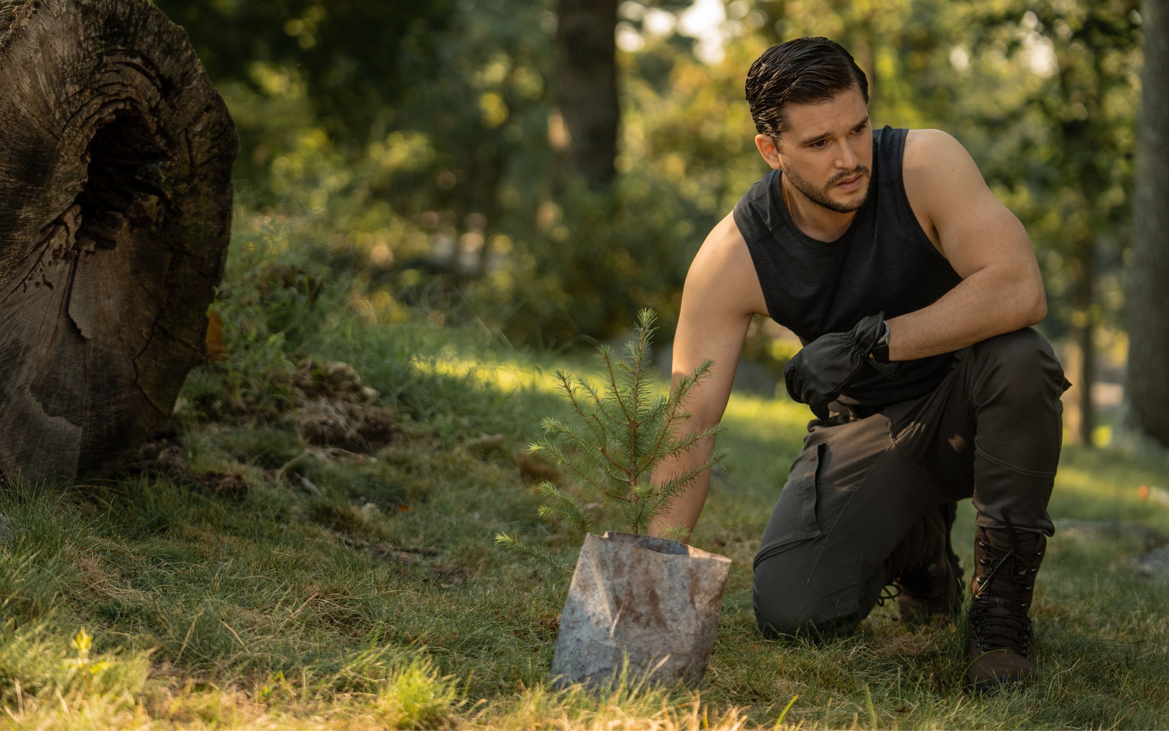 Kit Harington starring in Apple TV’s Extrapolations series. He is wearing black clothing and is in the woods beside a small sapling.