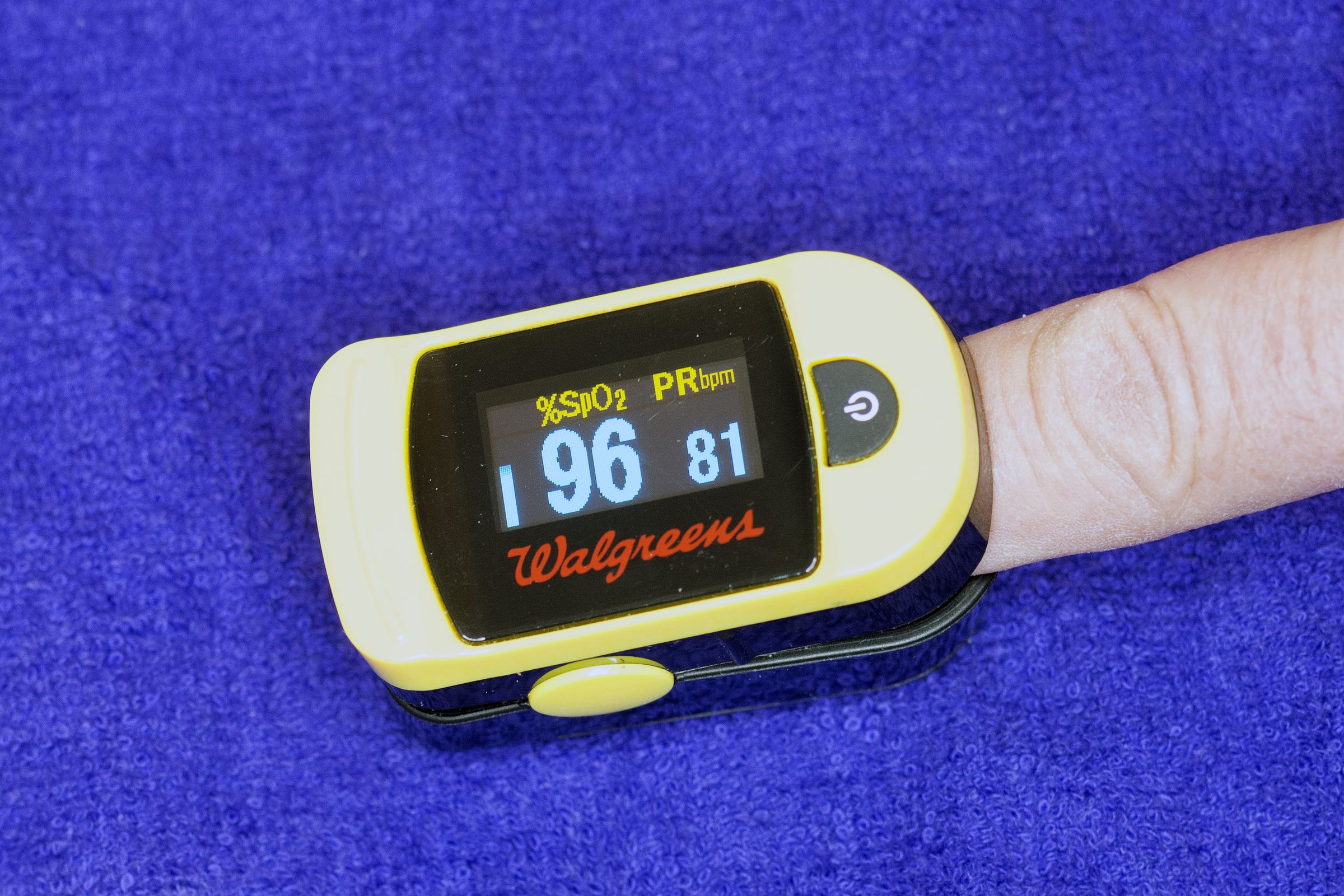 Pulse oximeter with the Walgreens logo clipped on a finger against a blue background.