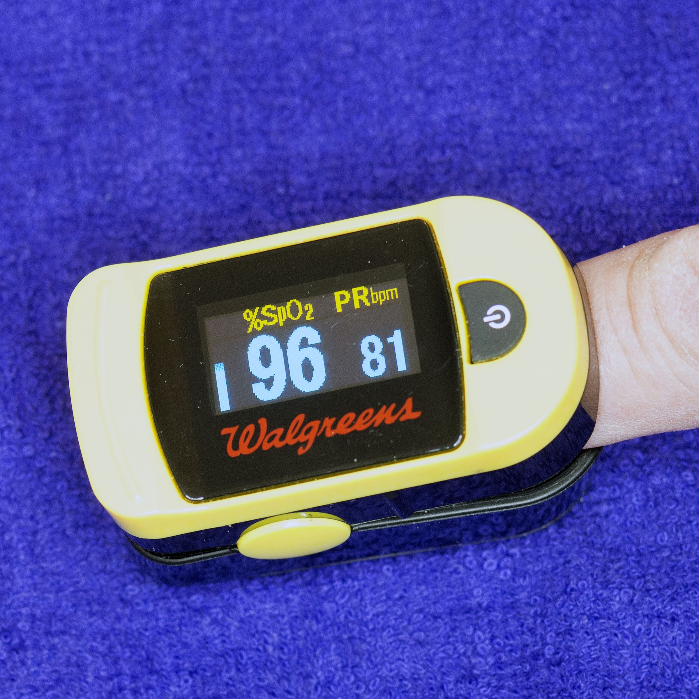 Pulse oximeter with the Walgreens logo clipped on a finger against a blue background.