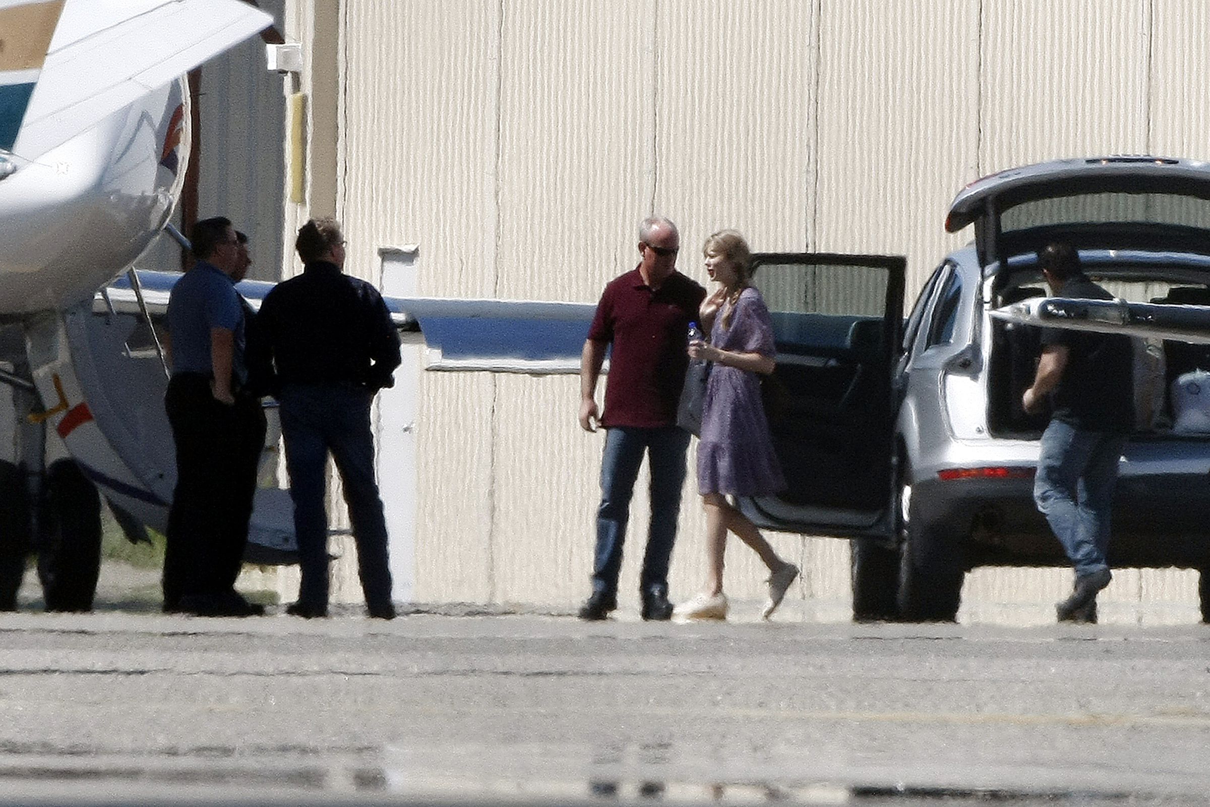 Taylor Swift at an airport walking from a vehicle toward a jet with other people standing nearby.