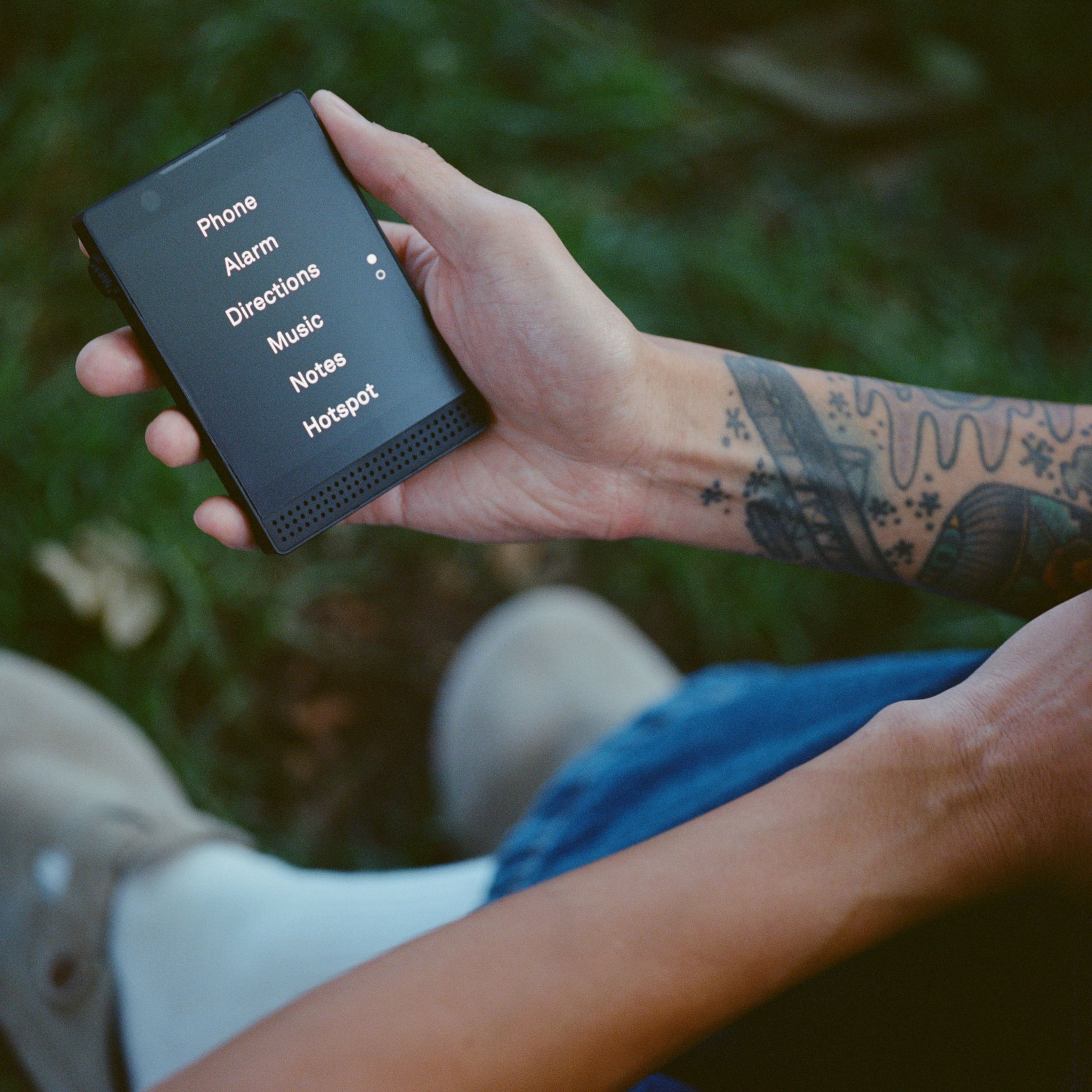 A person holding a Light Phone 3, over grass.