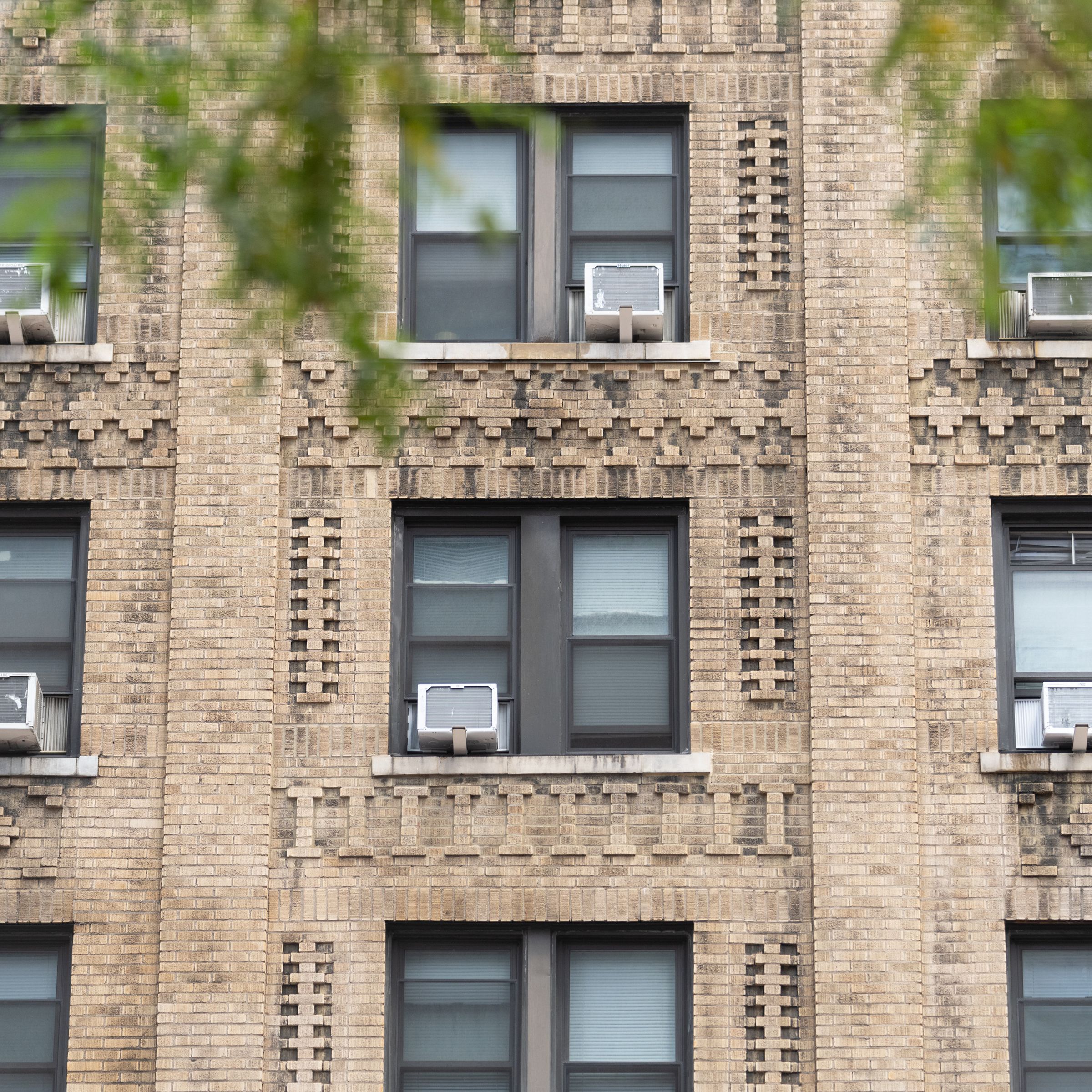 Three rows of windows on the side of an apartment building with air conditioning units jutting out from several windows. 