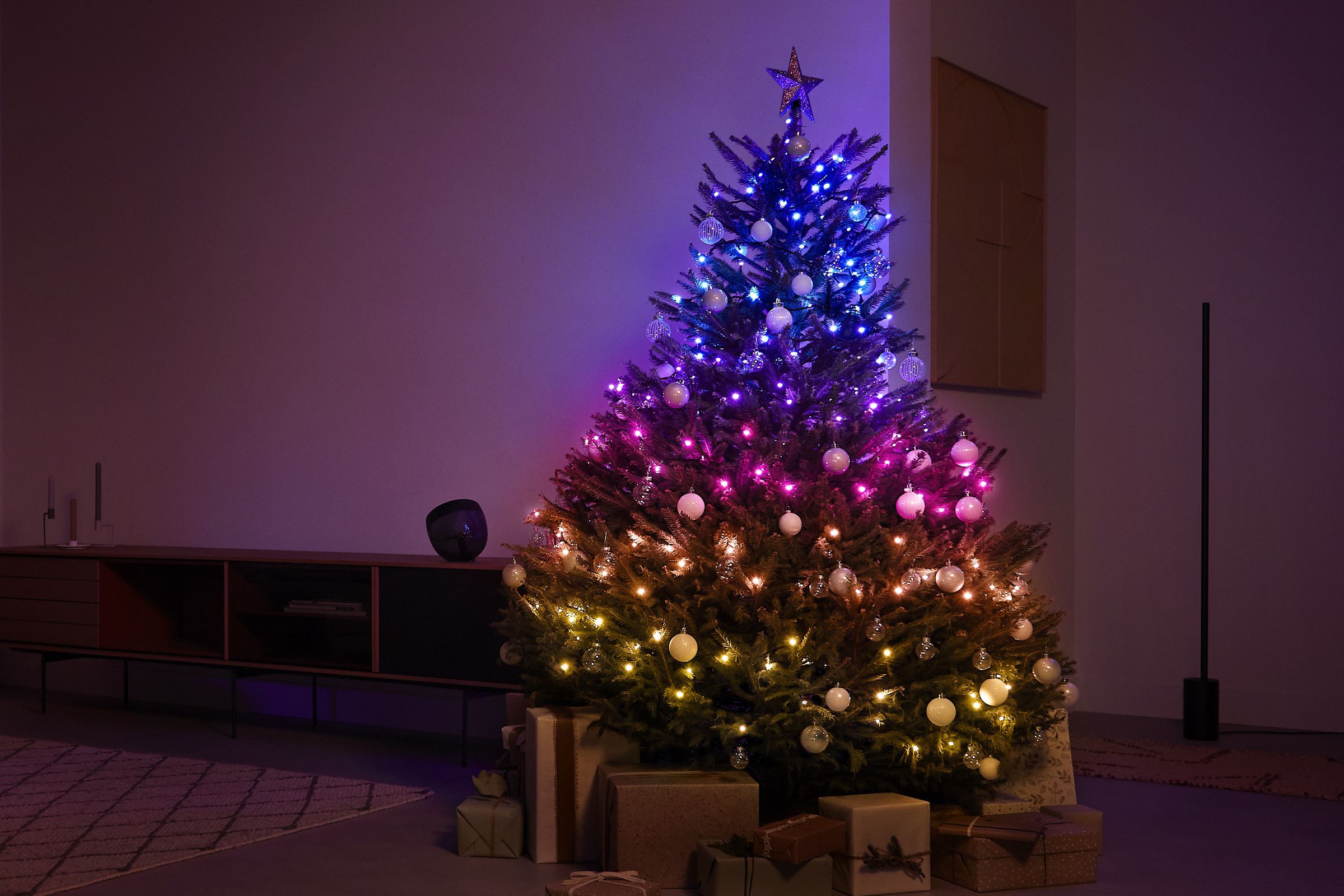 A Christmas tree in a living room lit up by colored smart lights.