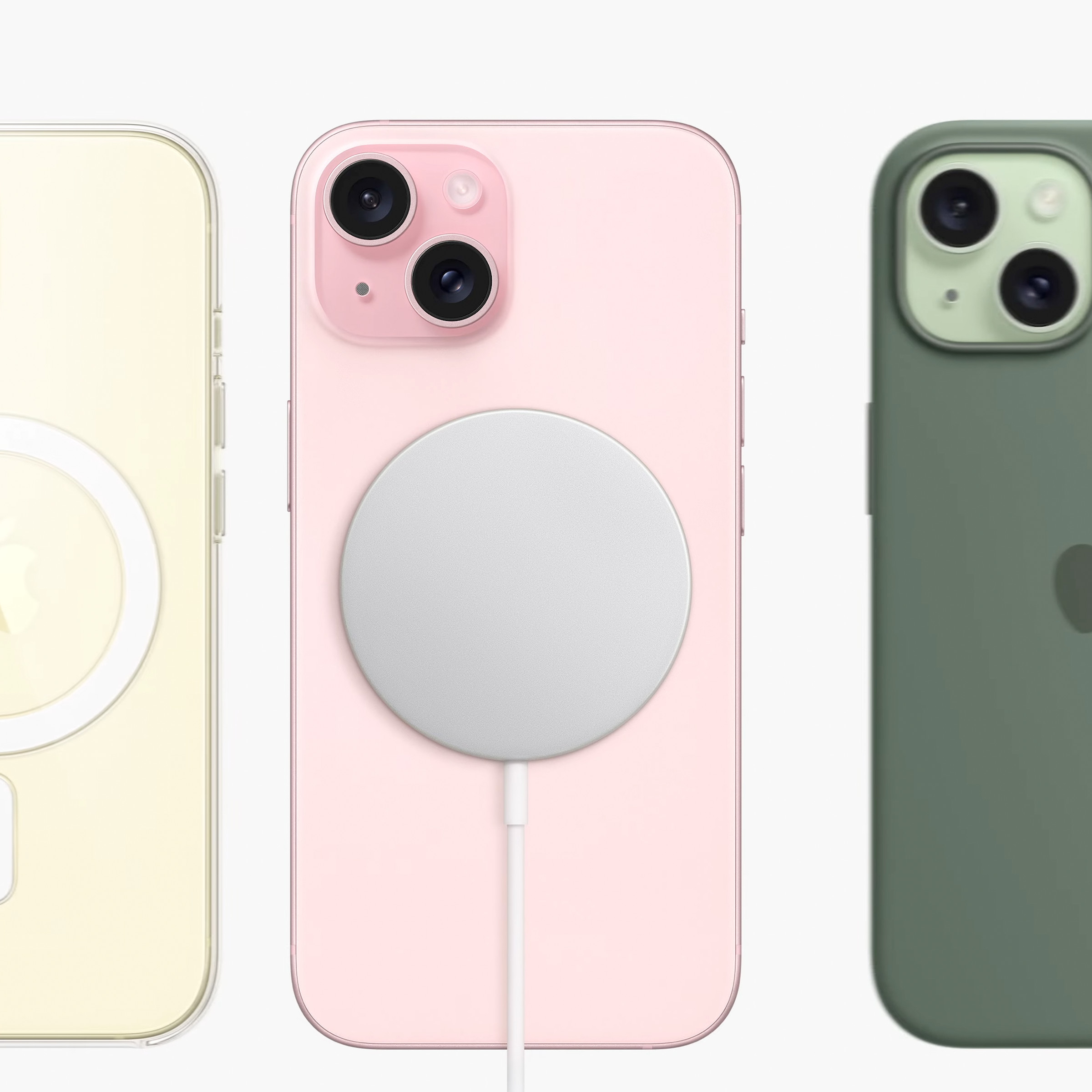 Rear shot of three iPhone 15 models: Yellow with a clear MagSafe case, pink with a magnetic charging puck on the back, and green with a green FineWoven case.