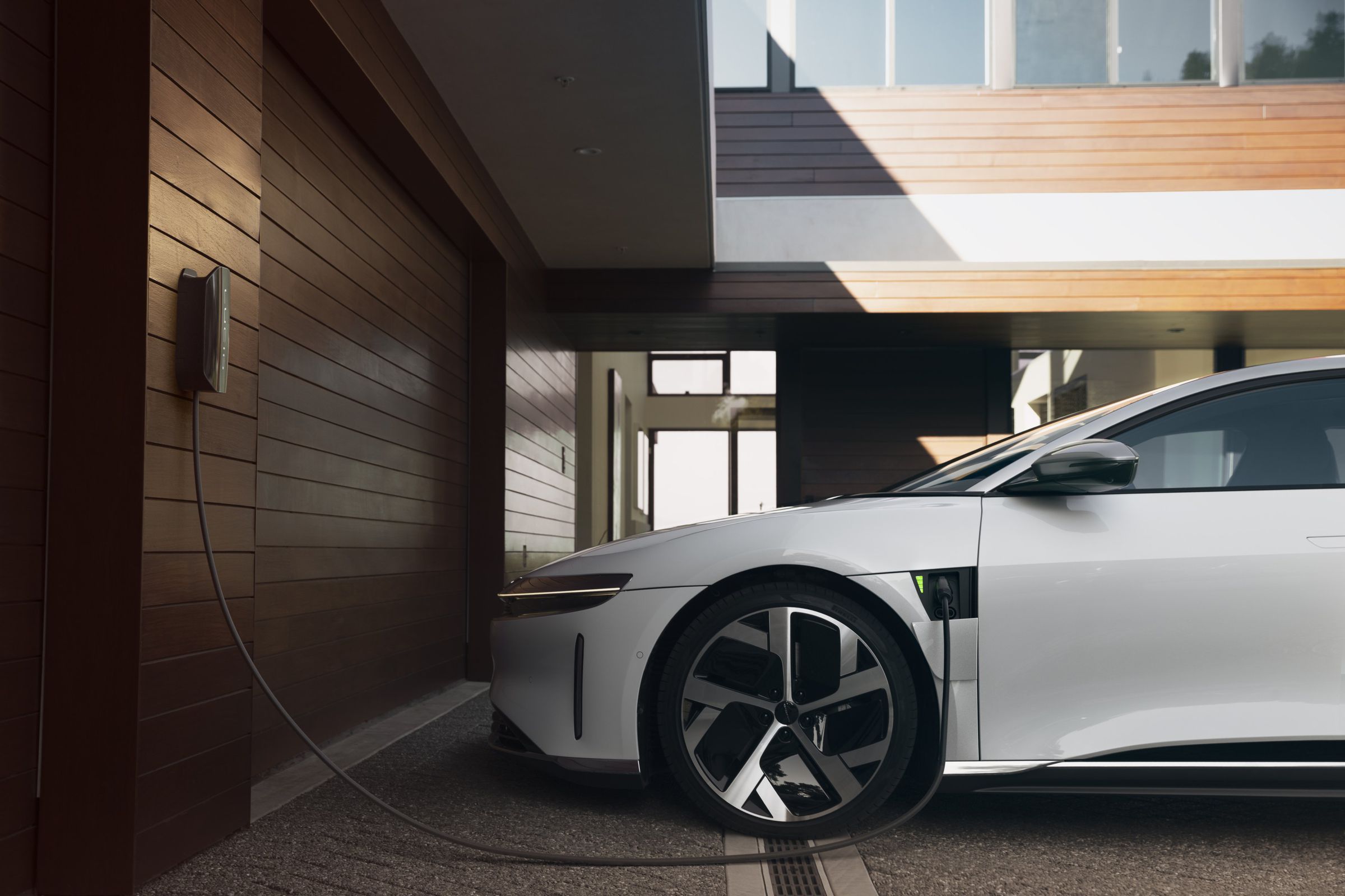 Lucid EV shown plugged into a wall charger outside a home with extensive wood paneling.