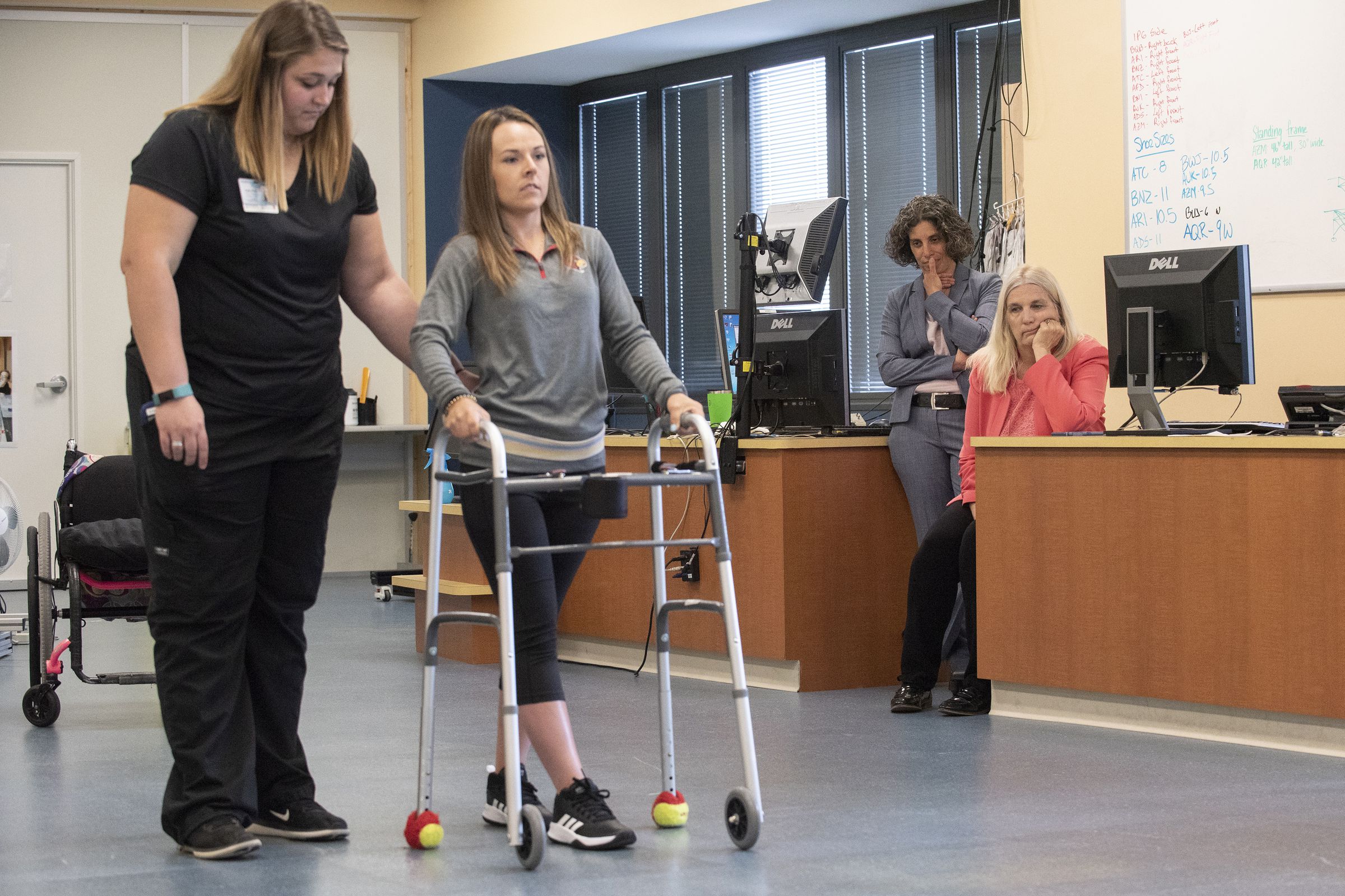 Kelly Thomas walking with a walker, as study authors Claudia Angeli and Susan Harkema look on. 