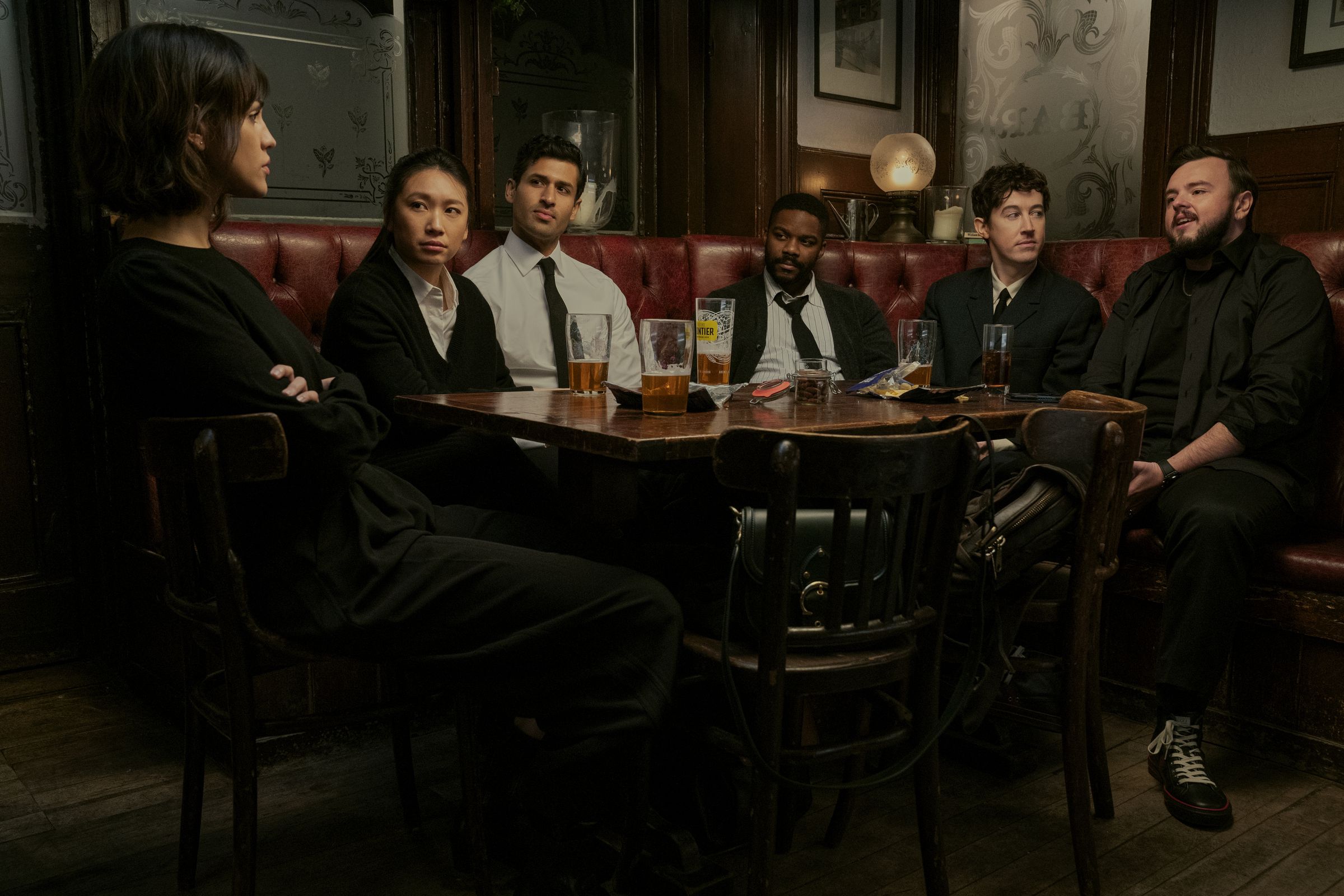 A group of six men and women wearing business attire, and sitting around a table in the booth of a bar.