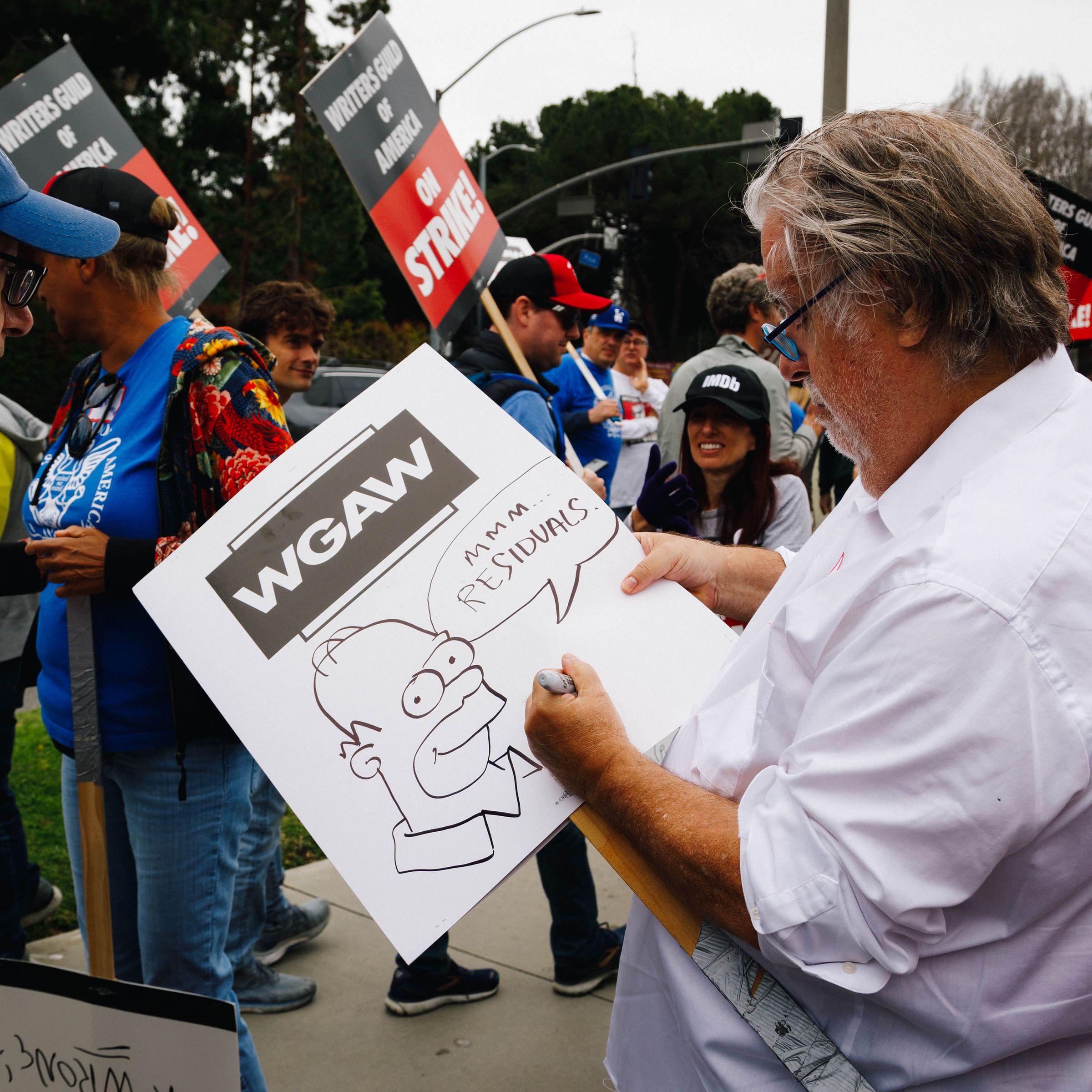 Simpsons creator Matt Groening drawing on a strike poster depicting Homer Simpson saying “mmm...residuals.”