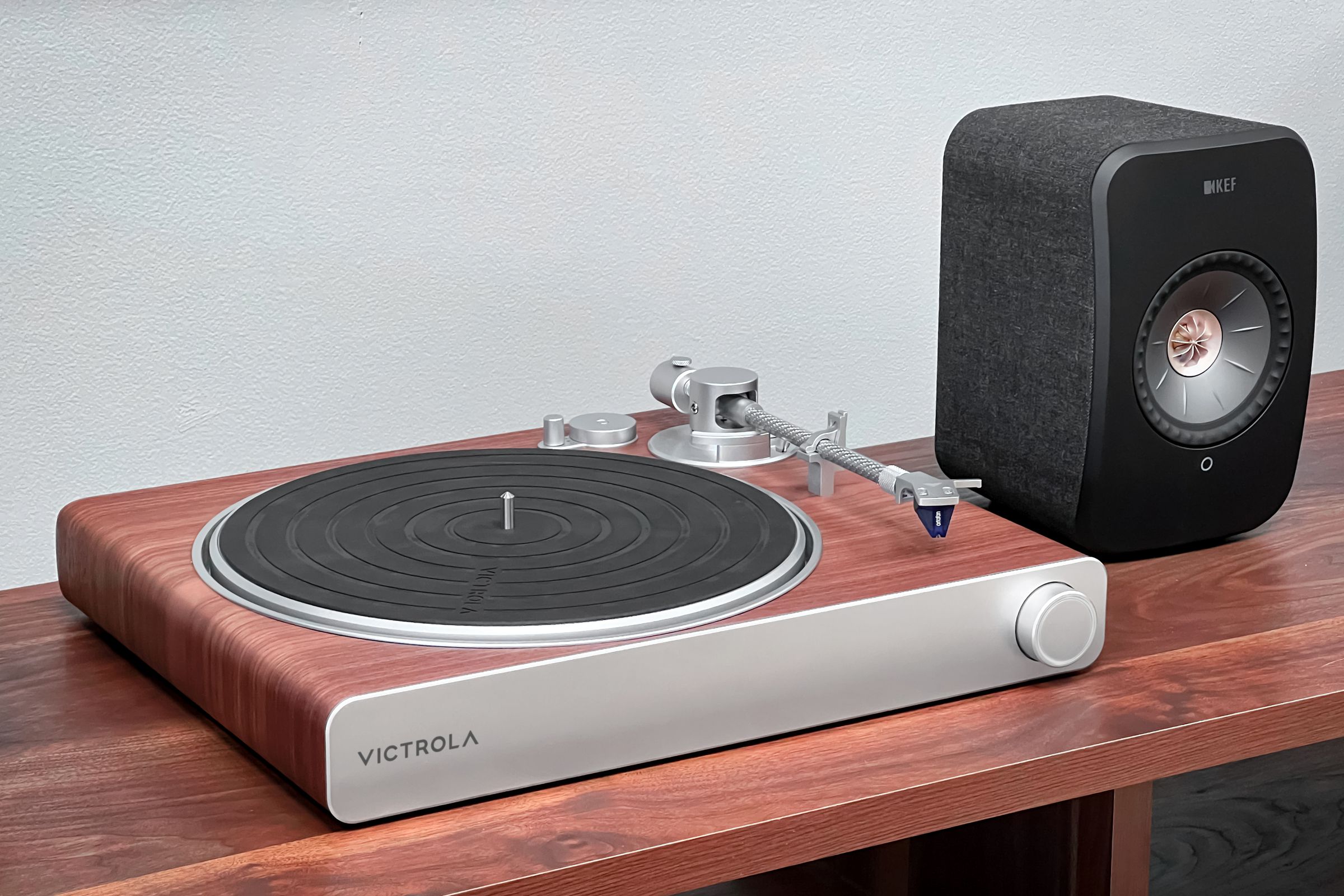 The new wooden Victrola Stream Sapphire turntable resting on a wooden table near a speaker.