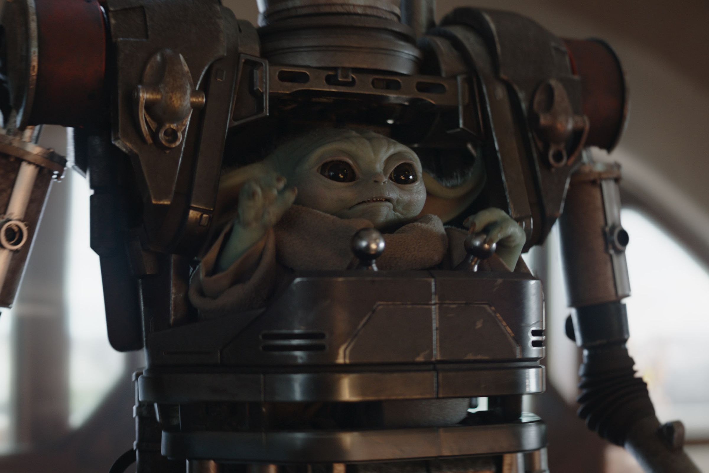 A small green gremlin-like creature wearing a burlap robe and sitting in the chest cockpit of a humanoid mobile suit of mechanical armor.