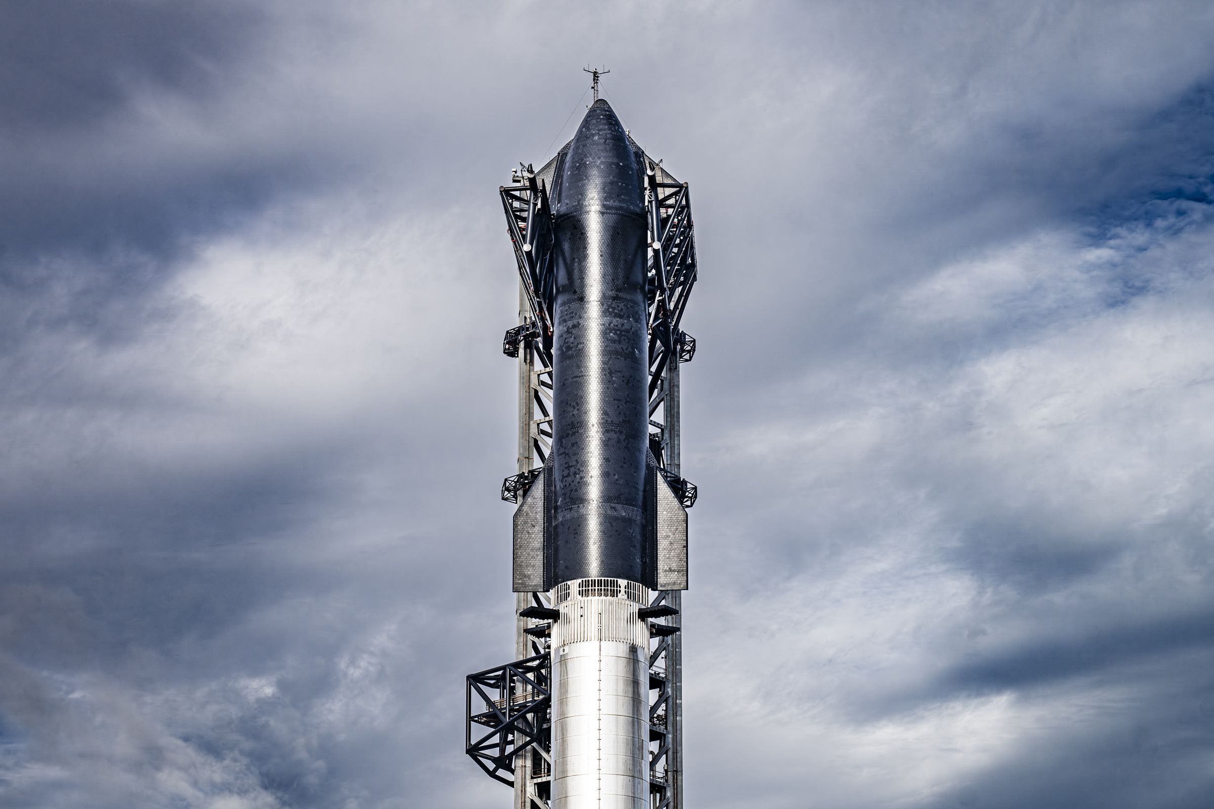 Image of the Starship prototype in position for a launch attempt against a background of a cloudy blue sky.