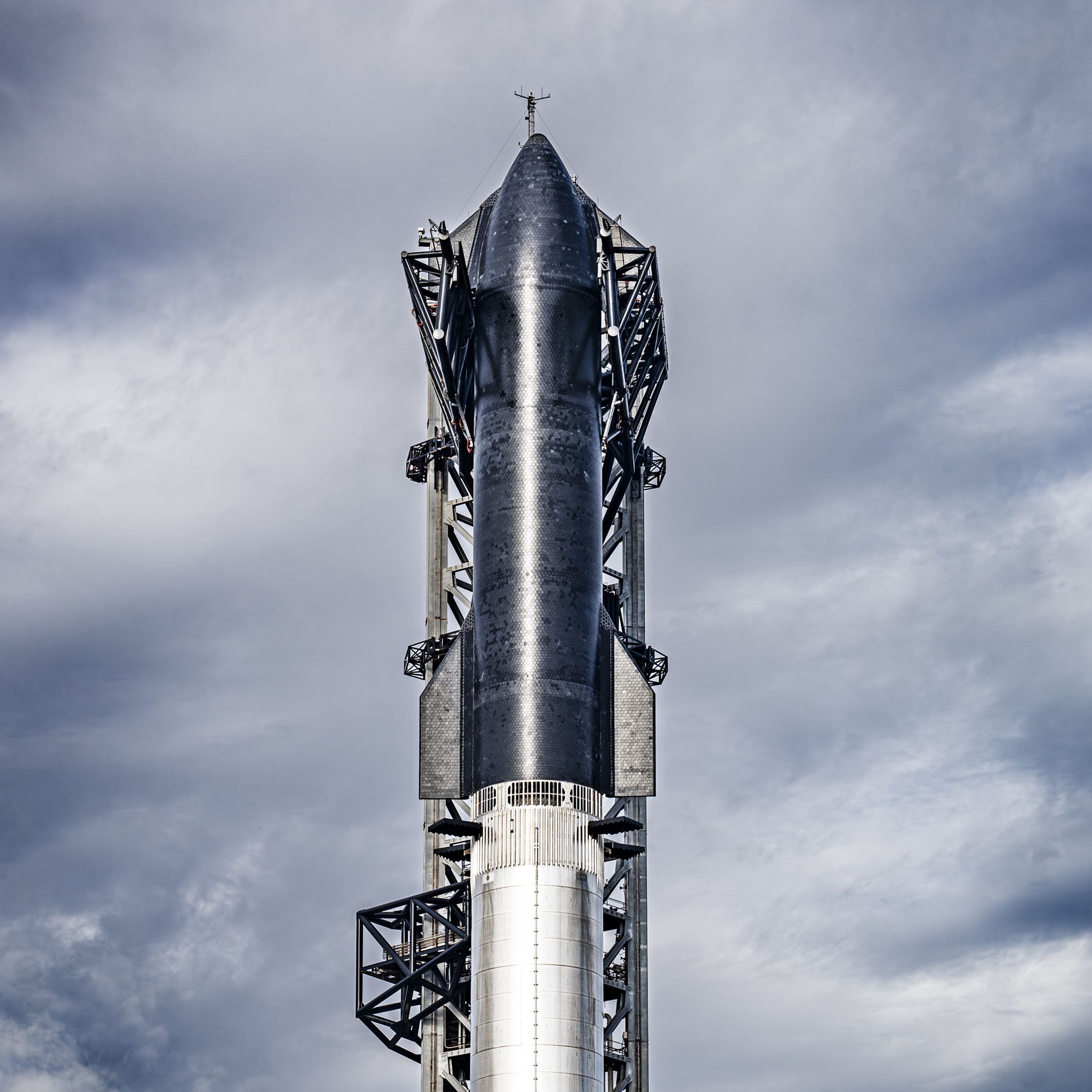 Image of the Starship prototype in position for a launch attempt against a background of a cloudy blue sky.
