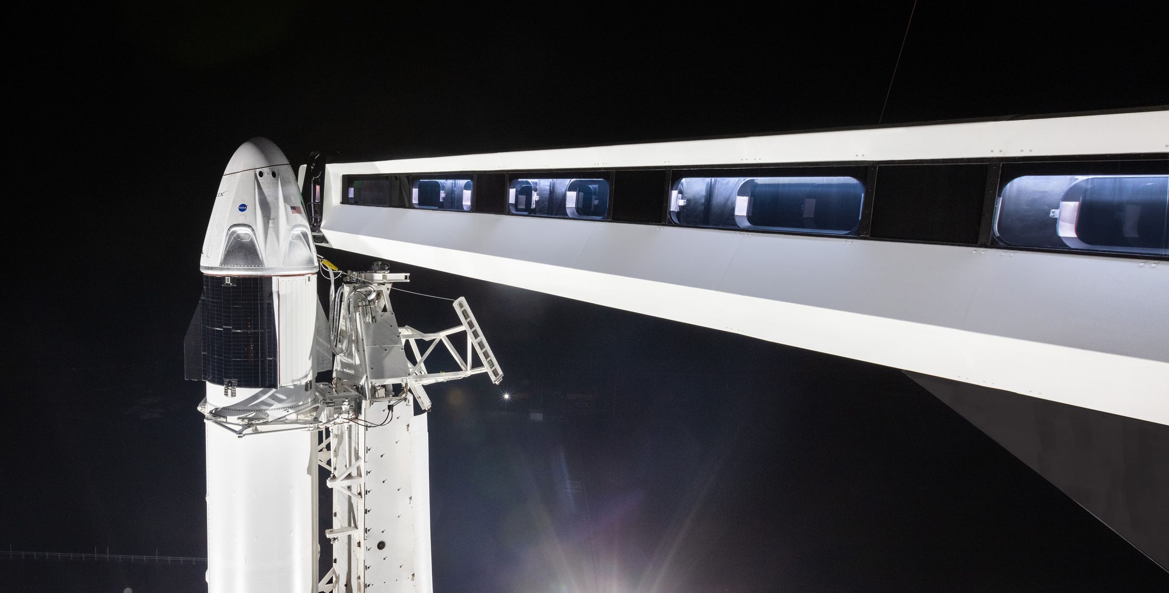 SpaceX’s Crew Dragon on top of the Falcon 9 that will carry it to space. SpaceX’s “crew access arm” is extended toward the capsule.