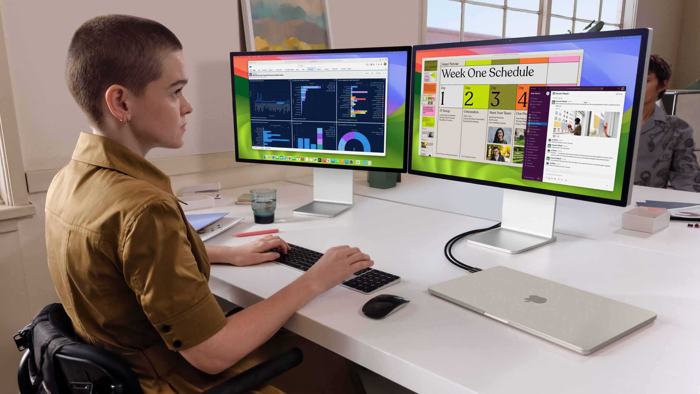 A person sitting at a desk using two monitors plugged into a closed MacBook Air.