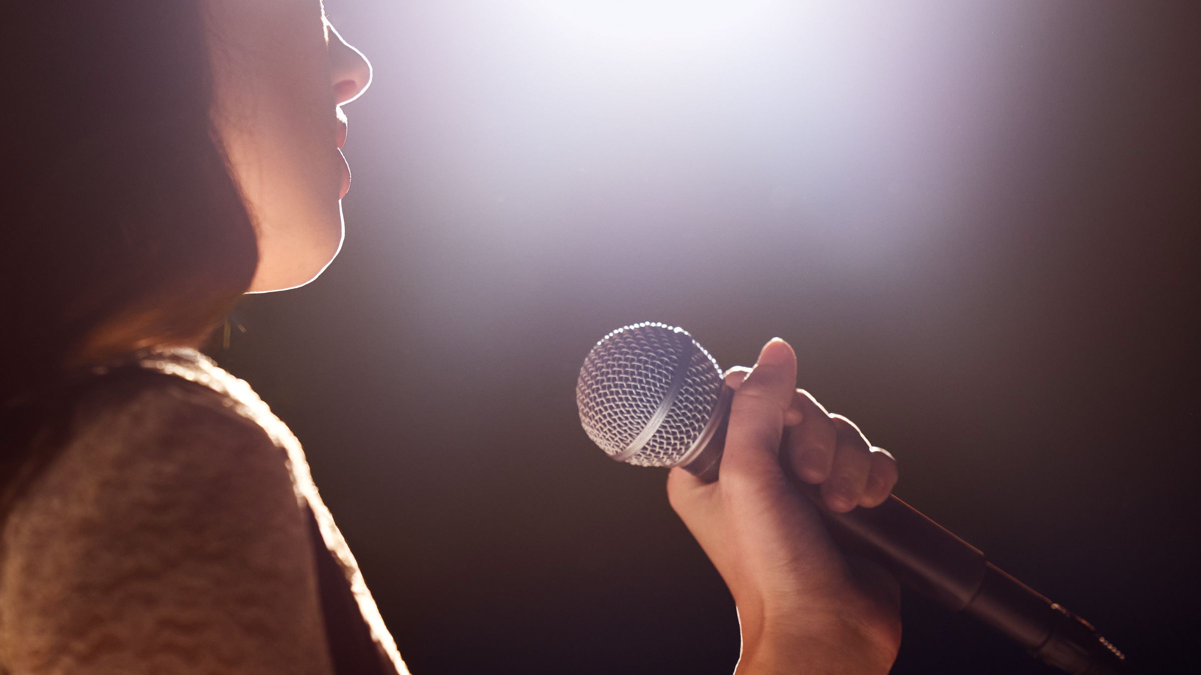 Someone singing into a microphone shown from behind with face obscured