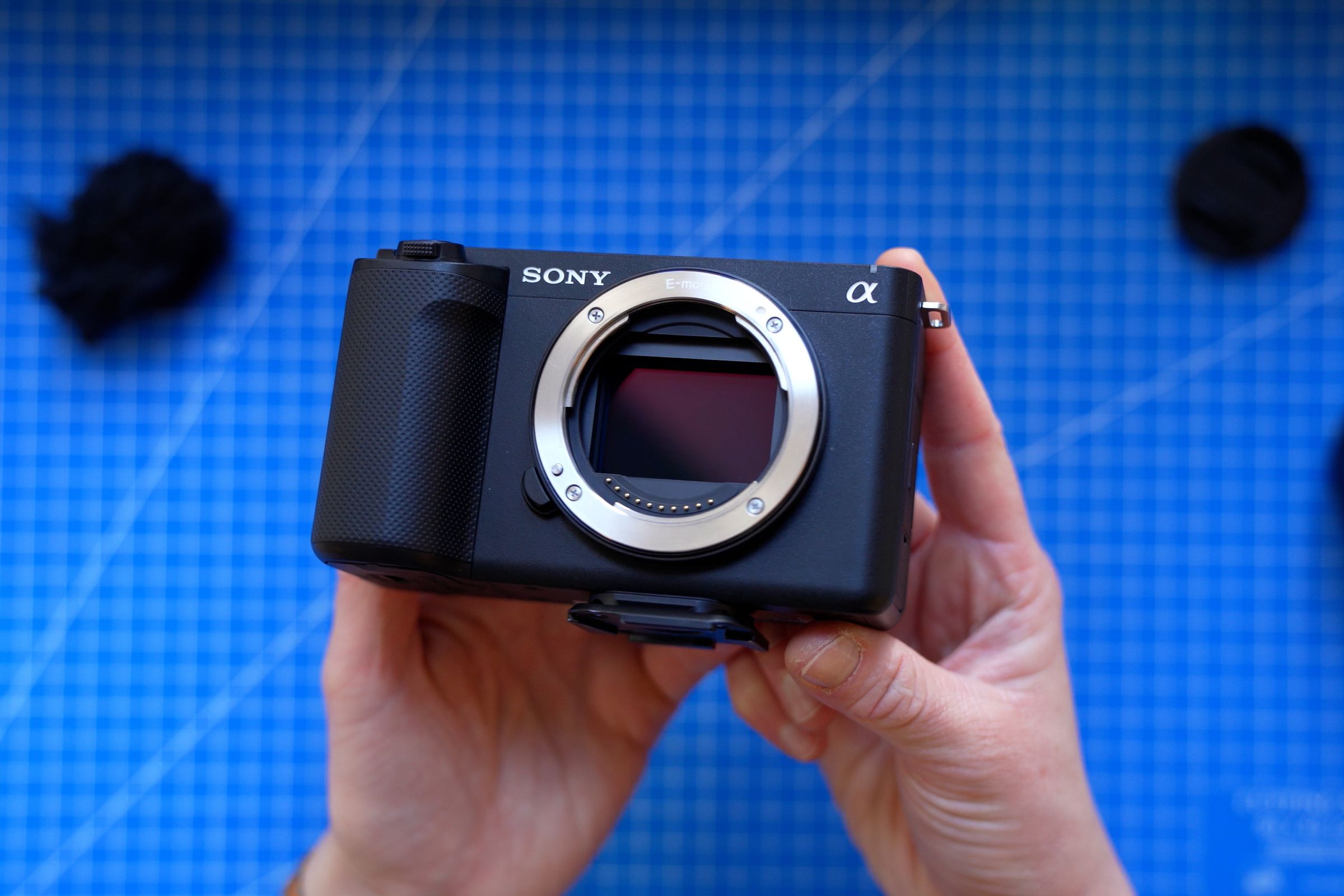 The Sony ZV-E1 camera without a lens attached, held up in a person’s hands above a blue cutting mat.