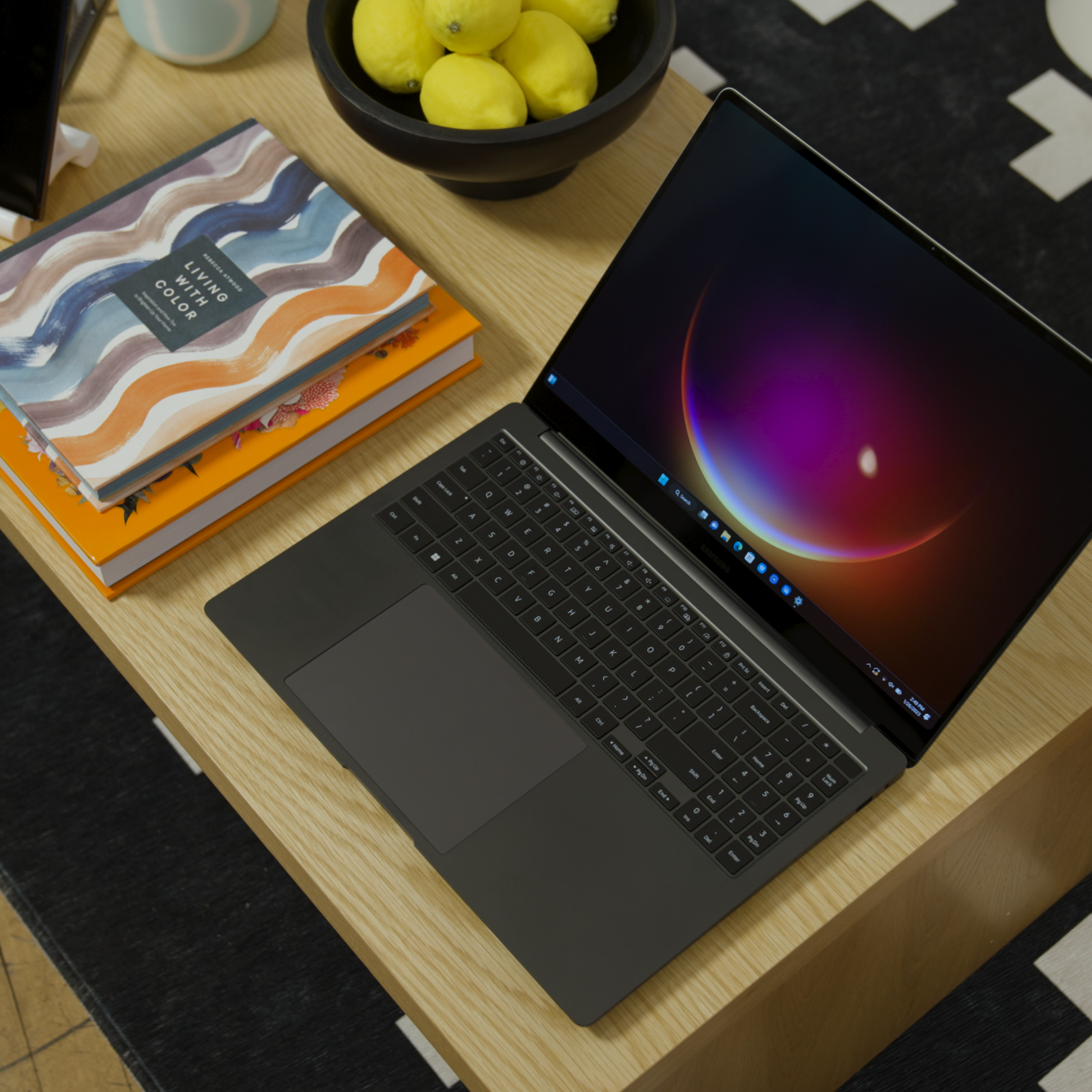 The Samsung Galaxy Book3 Ultra seen from above on a table next to a pile of books. The screen displays a half-Moon.