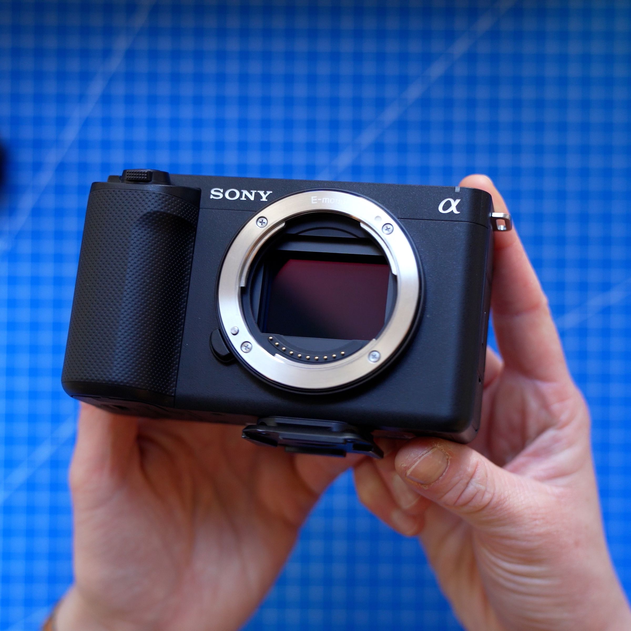The Sony ZV-E1 camera without a lens attached, held up in a person’s hands above a blue cutting mat.