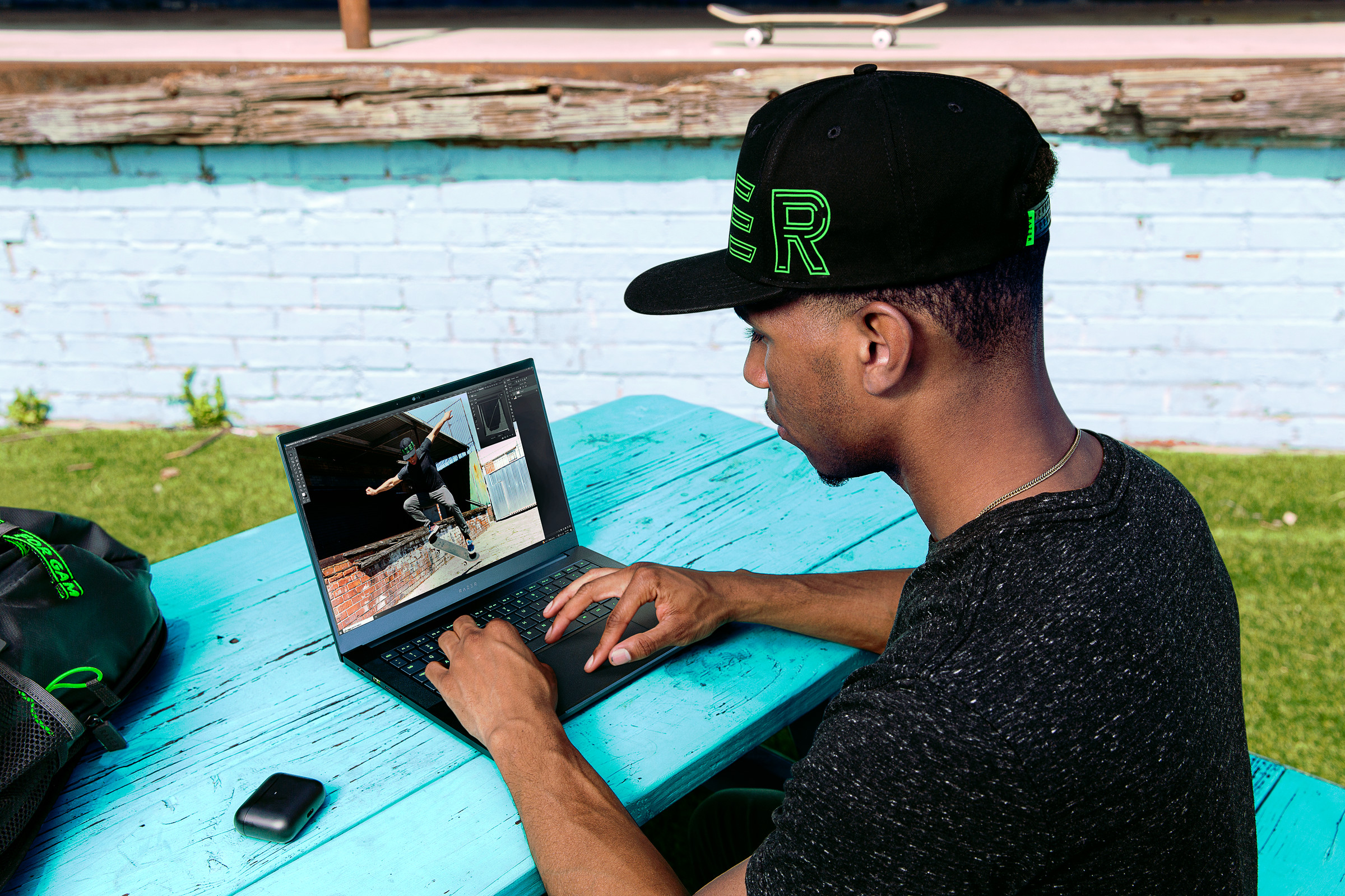A user types on the Razer Blade 14 black model, seated on a blue picnic table.