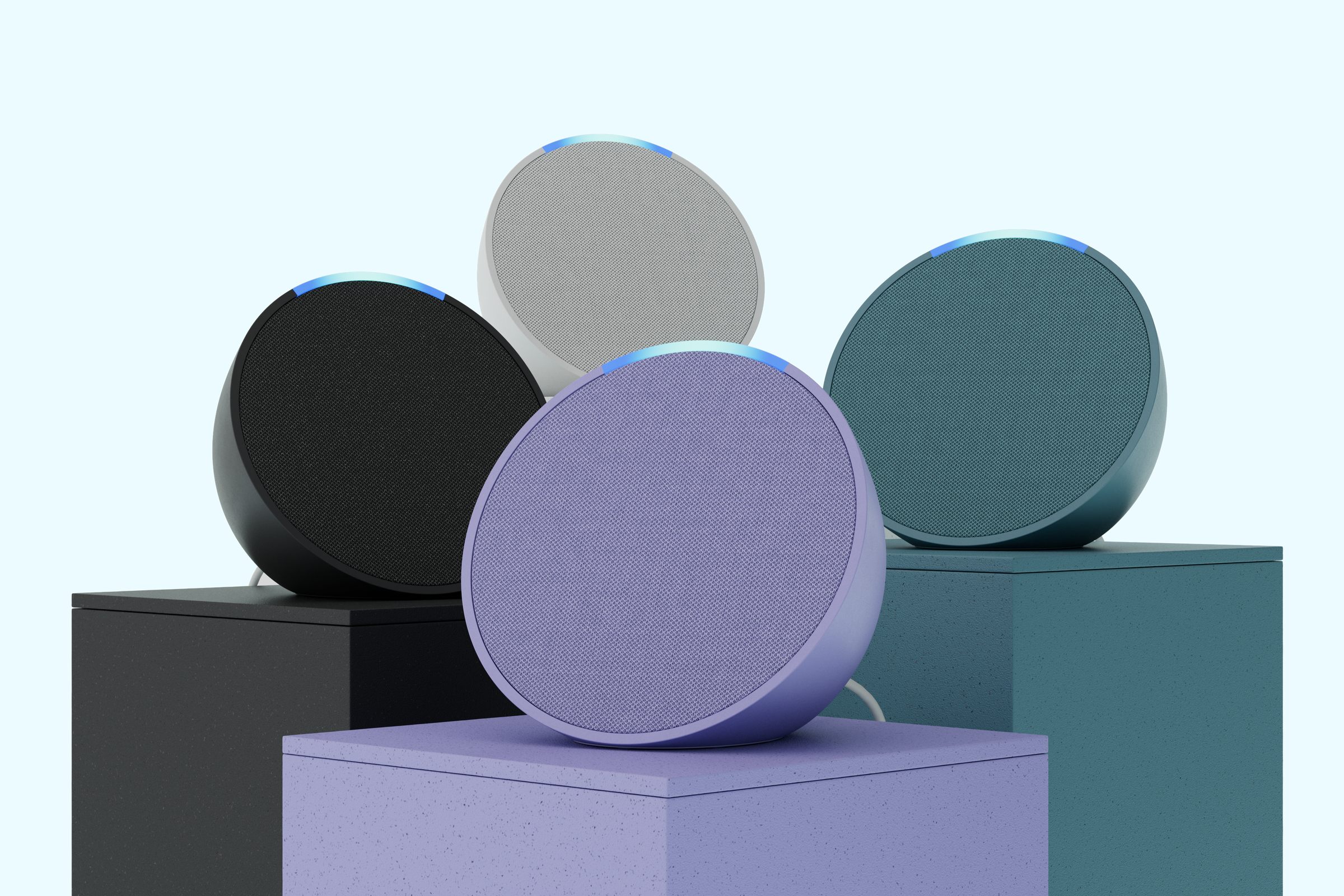 Four Echo Pop smart speakers in purple, green, black and white on matching colored stands.