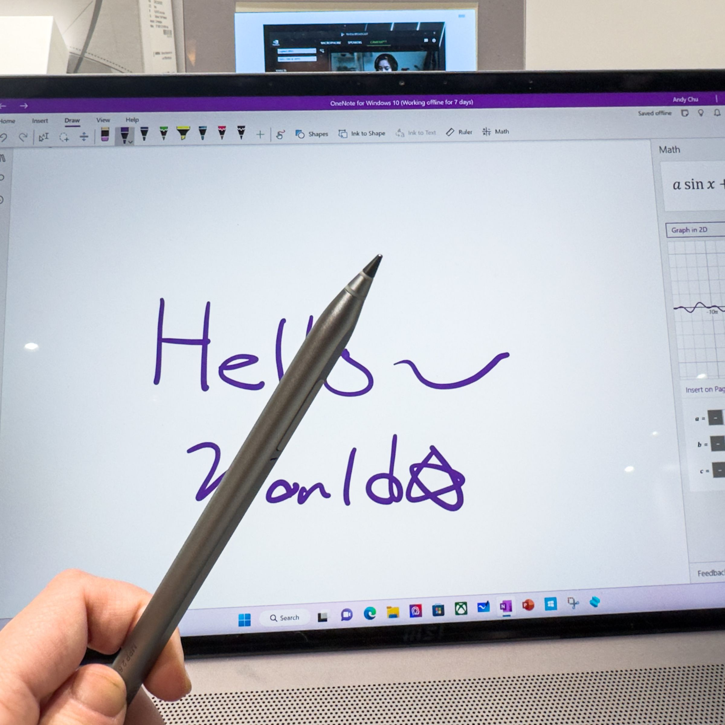 The MSI Pen 2 held in front of a computer screen where “Hello World” is written in Microsoft Paint.