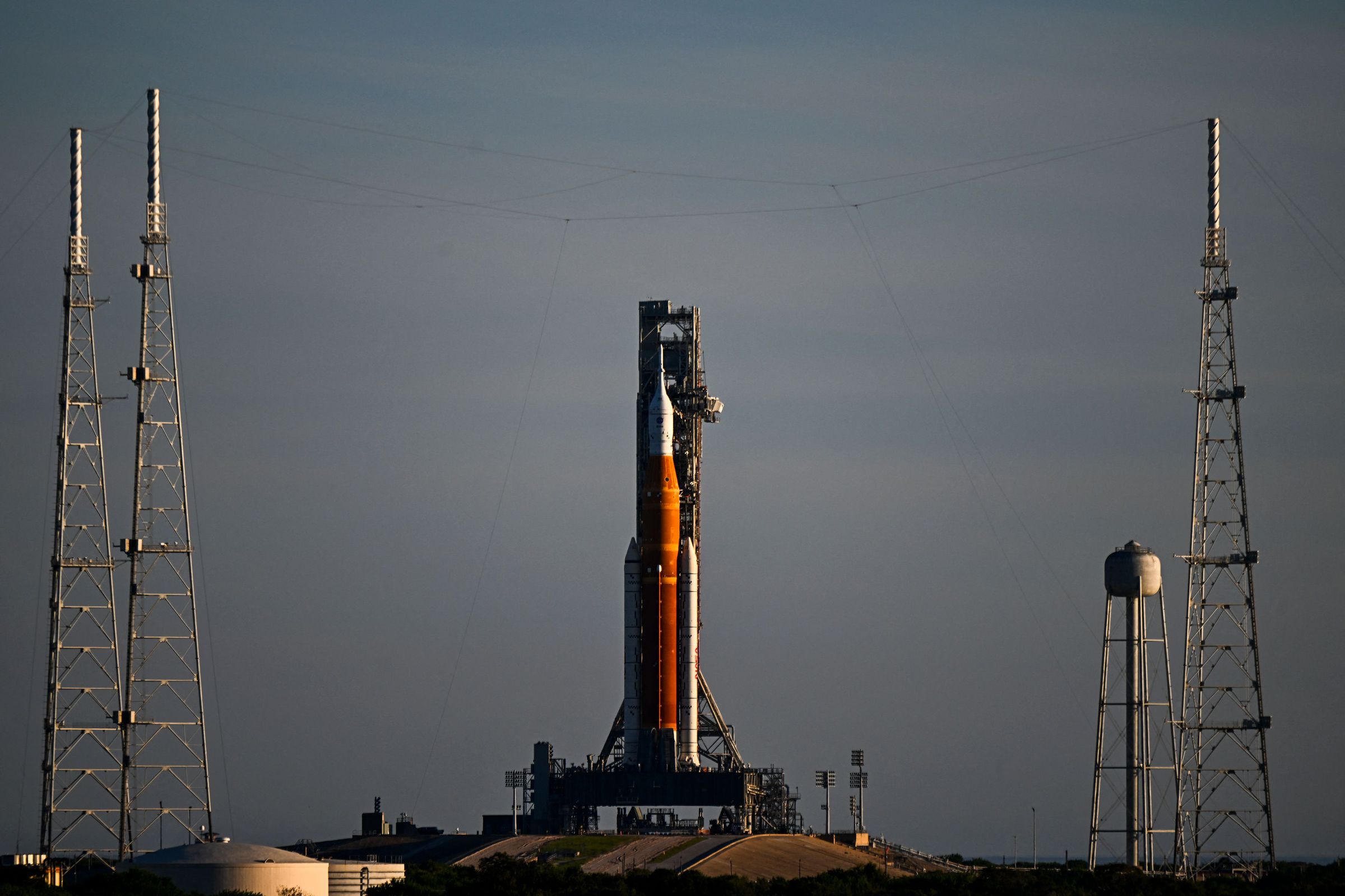 An orange and white rocket sits on a launchpad at the center of a landscape photo.