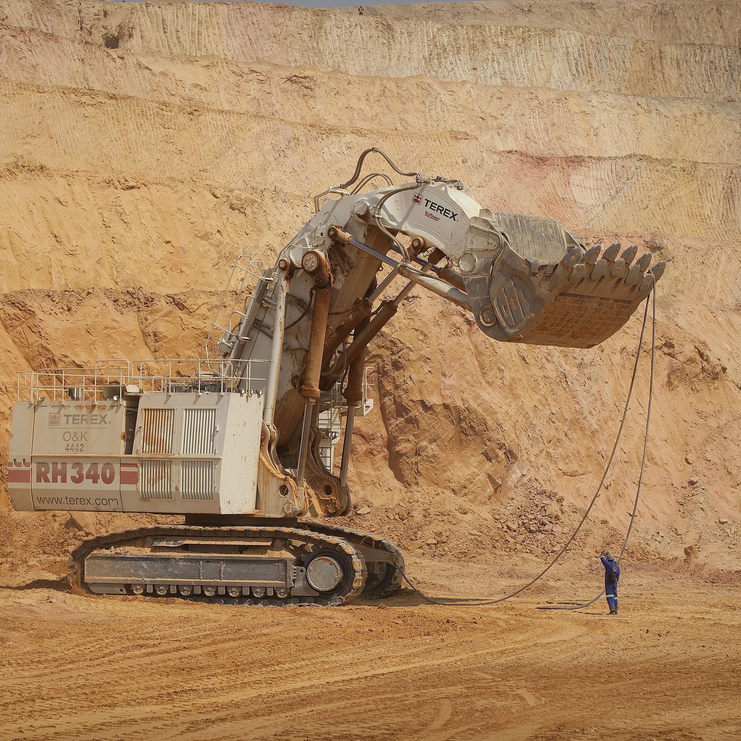 A person stands next to a giant mining excavator in an open pit mine.