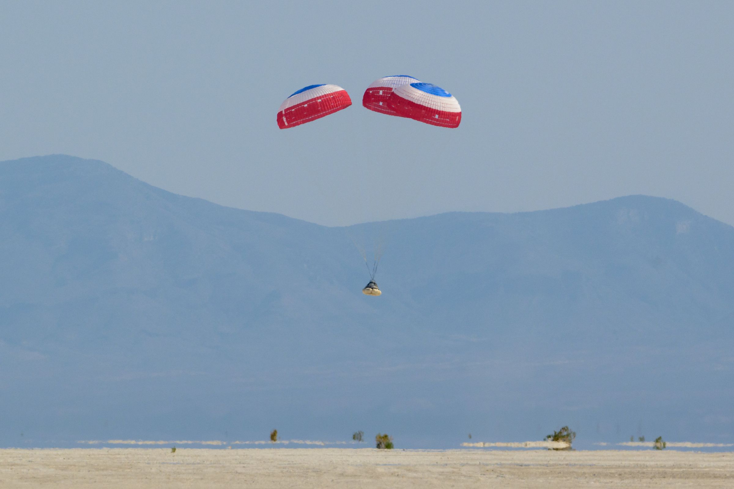 Boeing’s Starliner spacecraft landing under parachutes in the New Mexico desert