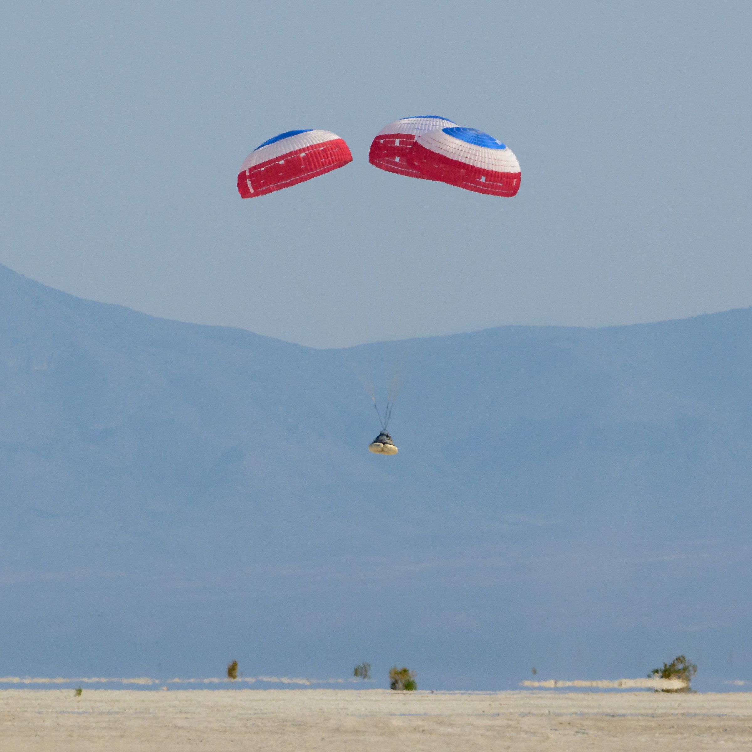 Boeing’s Starliner spacecraft landing under parachutes in the New Mexico desert