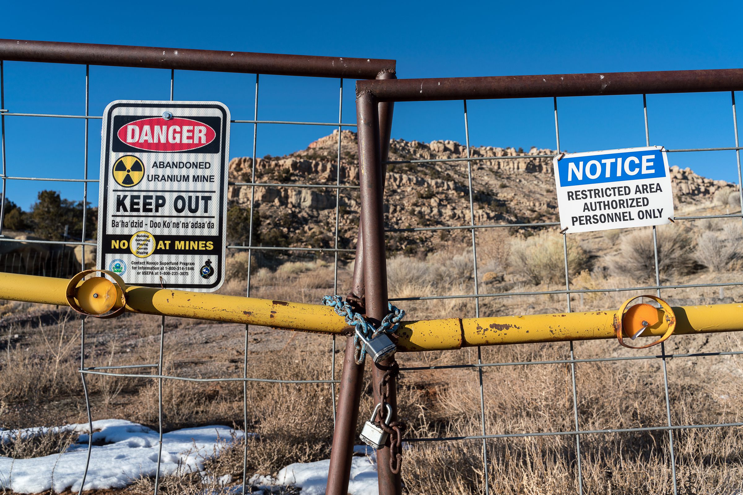Two warning signs are posted on a gate that’s been chained shut. A sign on the left reads: “Danger Abandoned Uranium Mine Keep Out.” Another sign on the right says: “Notice Restricted Area Authorized Personnel Only.”