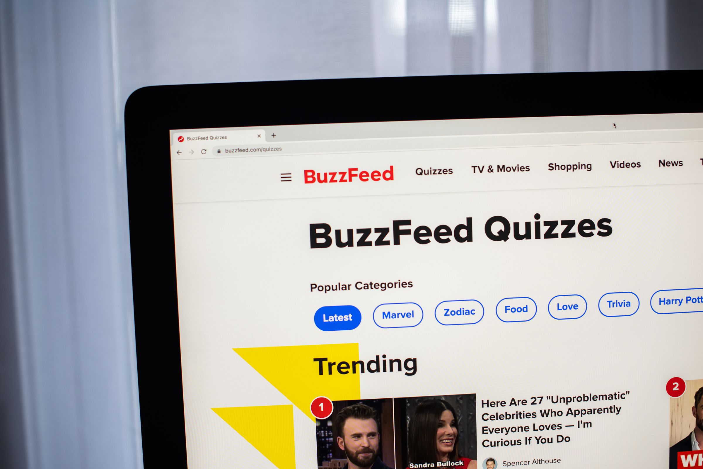 A photograph of a laptop screen showing the BuzzFeed Quizzes homepage. 