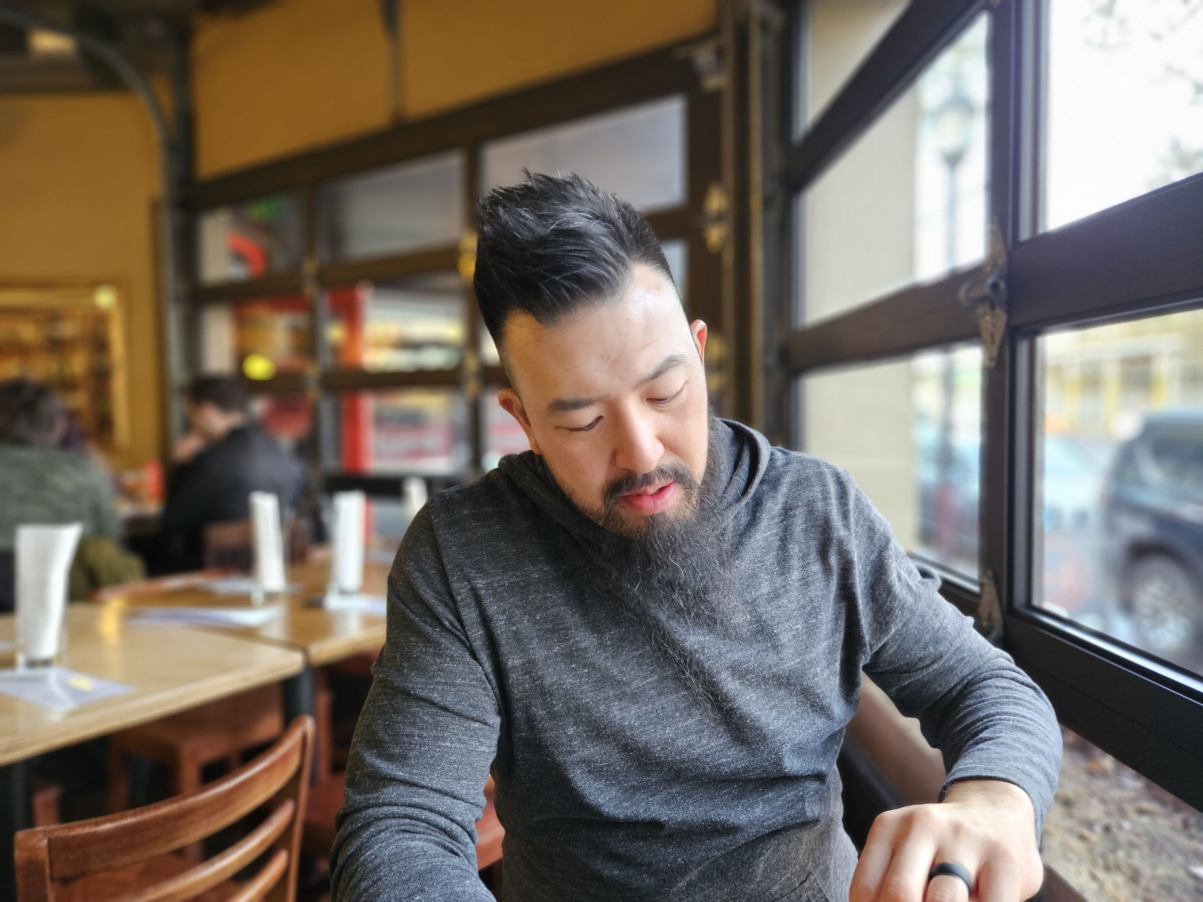 Portrait mode photo of a man sitting at a table in a restaurant with a large window to his left.