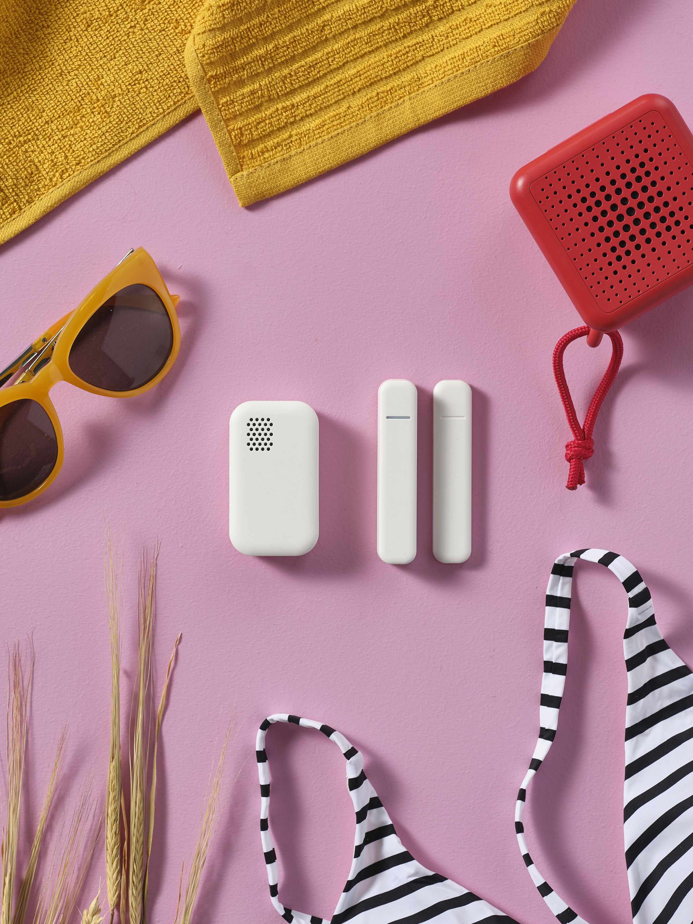 Ikea’s new white Badring and Parasoll sensors on a pink table surrounded by beach gear like sunglasses and bikini.