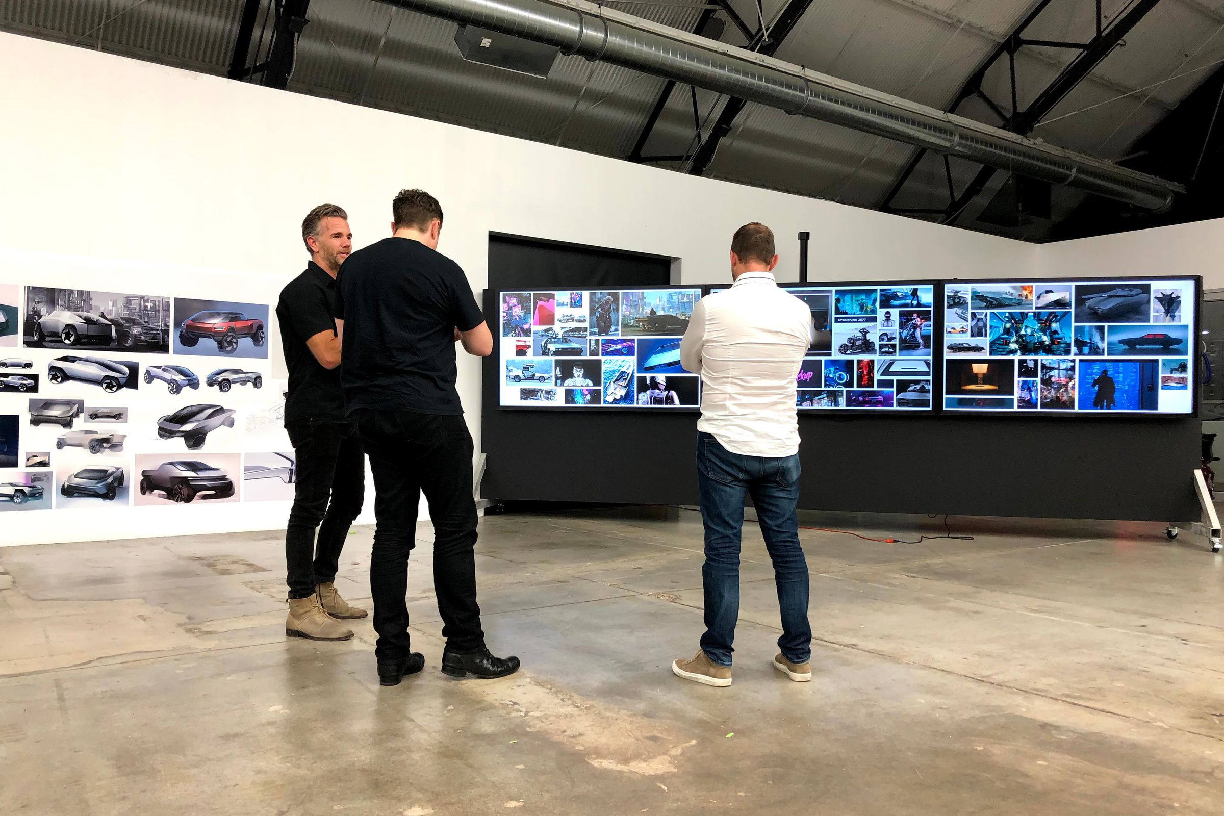 Musk, von Holzhausen, and a third man stand in front of several boards of images.