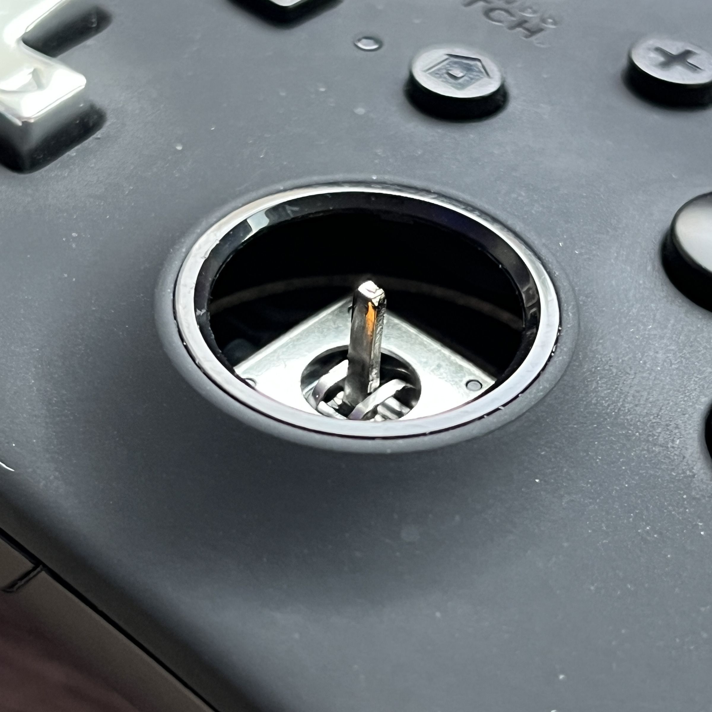 Close-up of the hole where the right joystick cover should be, but now there’s an analog mechanism with a skinny metal rod protruding out. Visible face buttons are the B, Y, home, and plus buttons along with a silver directional pad on a matte black controller.
