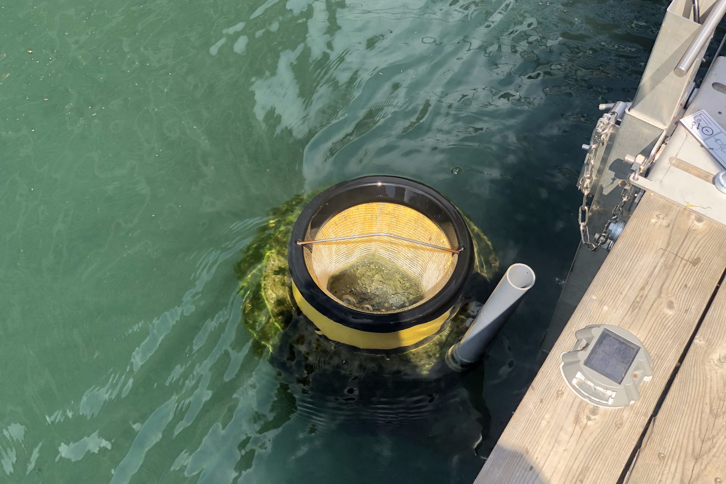A yellow bin floats in the water next to a wooden dock