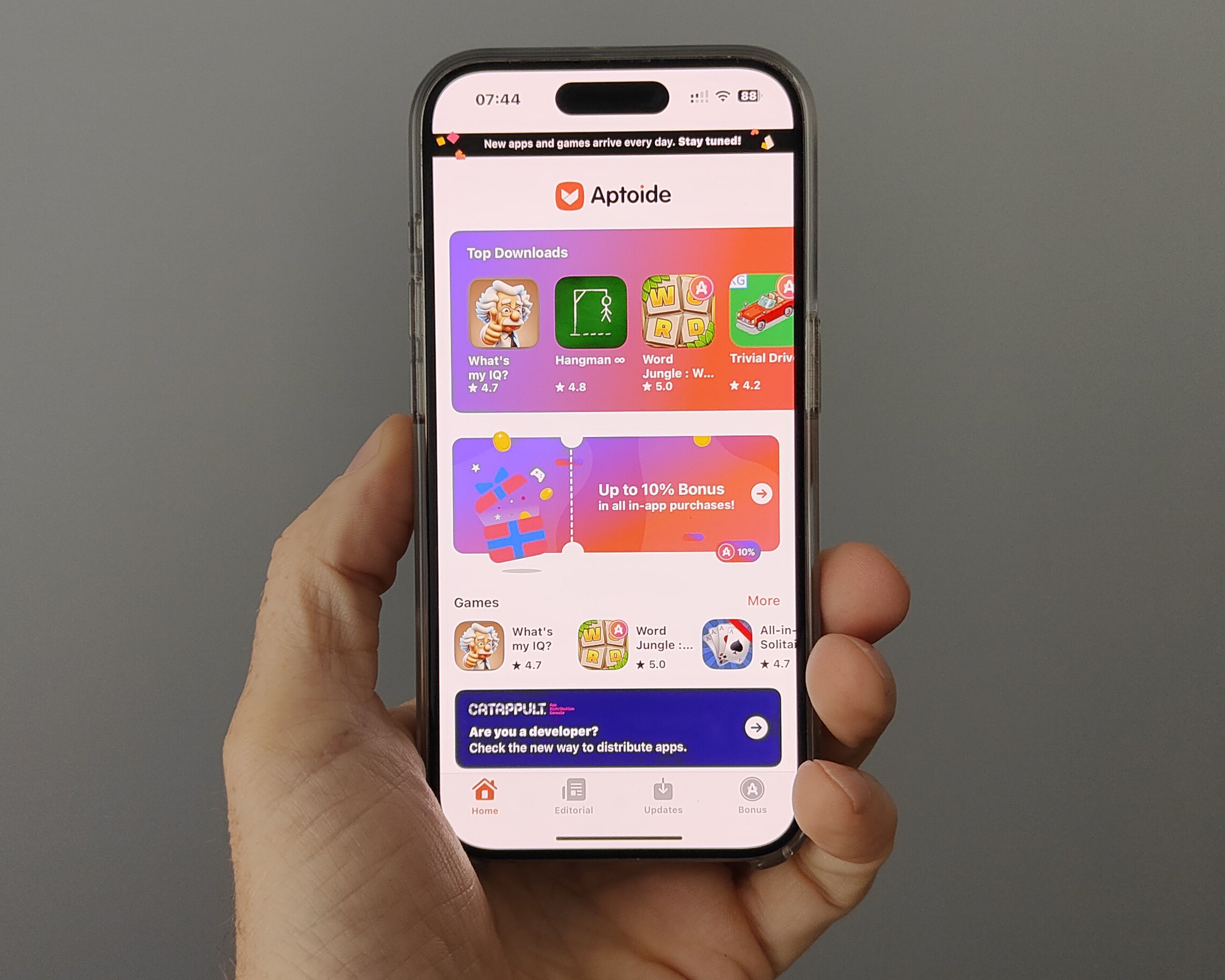 An iPhone held aloft in one hand shows the Aptoide iOS game store landing page full of colorful icons for the few games available.
