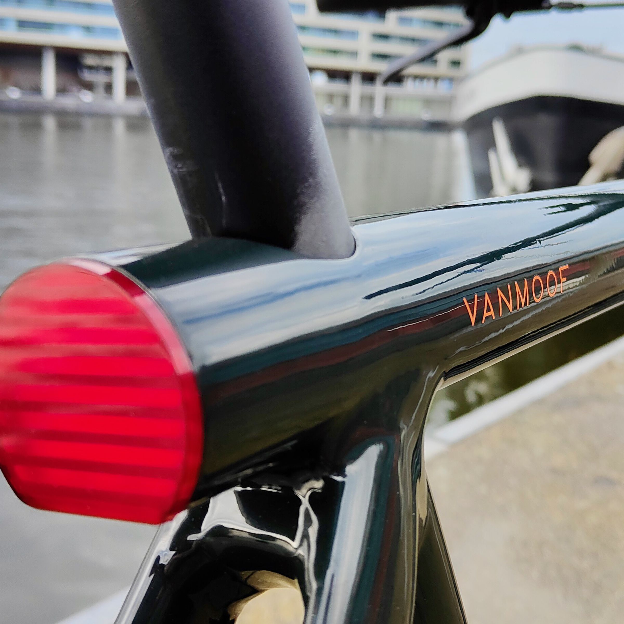 A zoomed in photo of a VanMoof e-bike from the rear light looking past the VanMoof logo and down the top tube to a distant ship on the horizon.