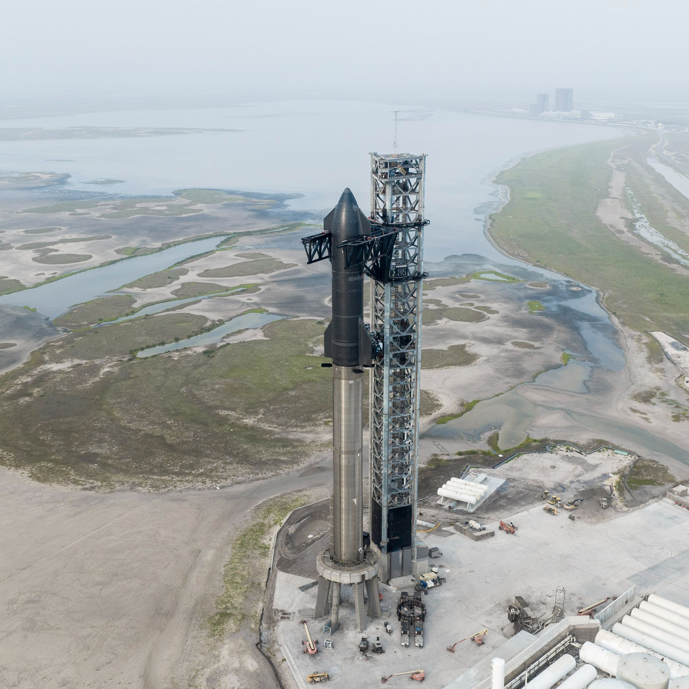 Zoomed-out landscape of SpaceX’s Starbase in Boca Chica, Texas, showing a water landscape in the back and the rocket front and center.