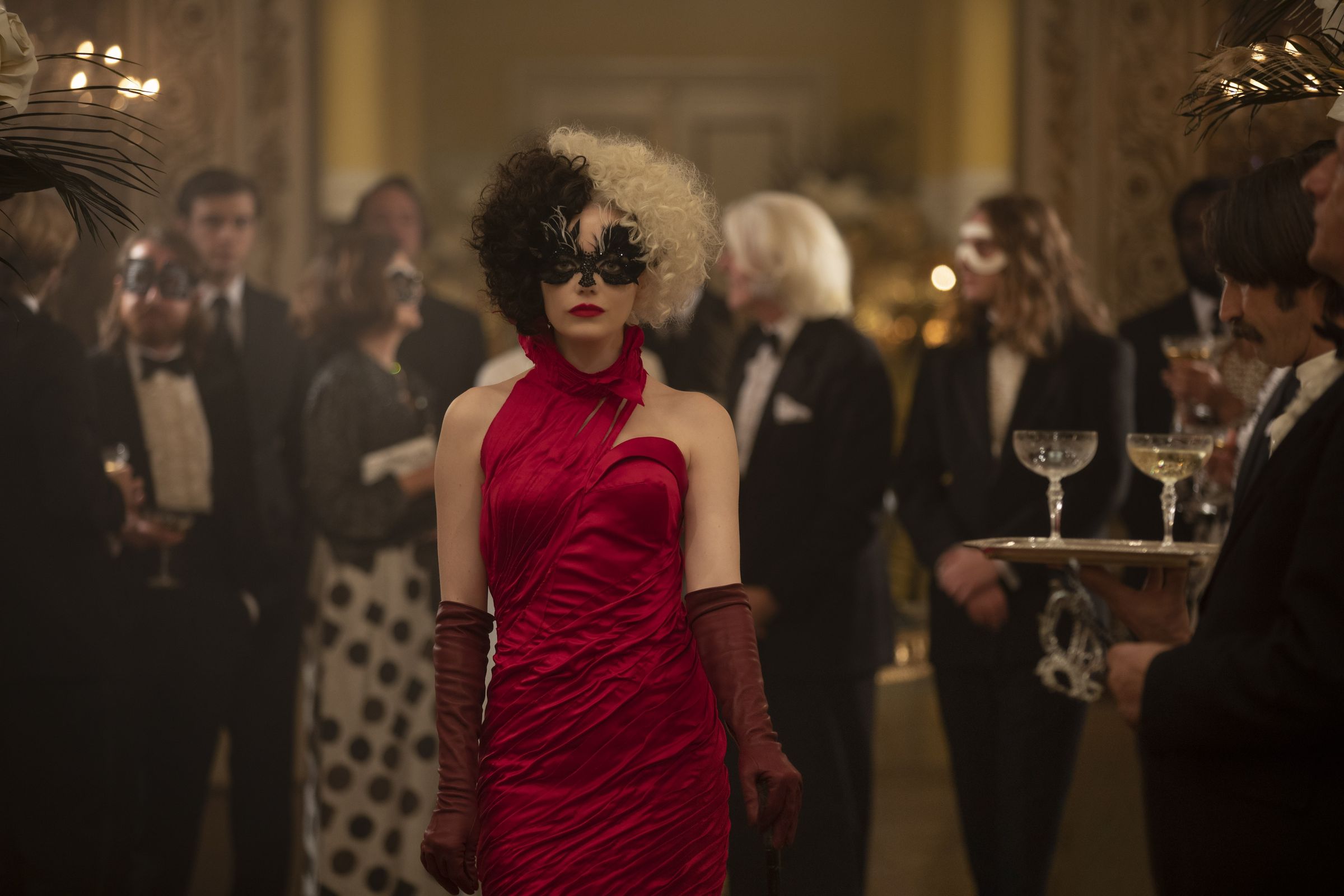 Emma Stone as Cruella de Vil in a red gown surrounded by party goers dressed entirely in black and white.