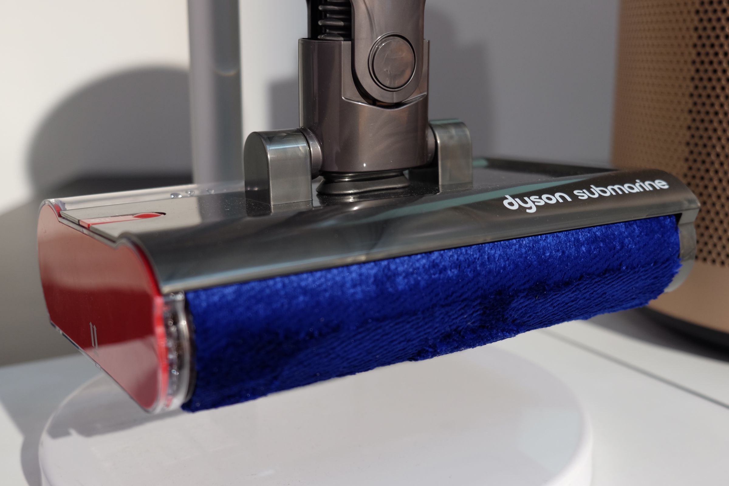 A close-up of the mopping attachment. It is rectangular, with a padded roller in front and a water tank in back.