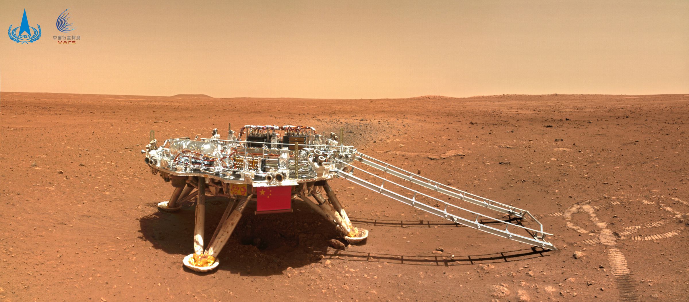 A landing platform with a ramp coming down from it sits among a red-orange landscape.